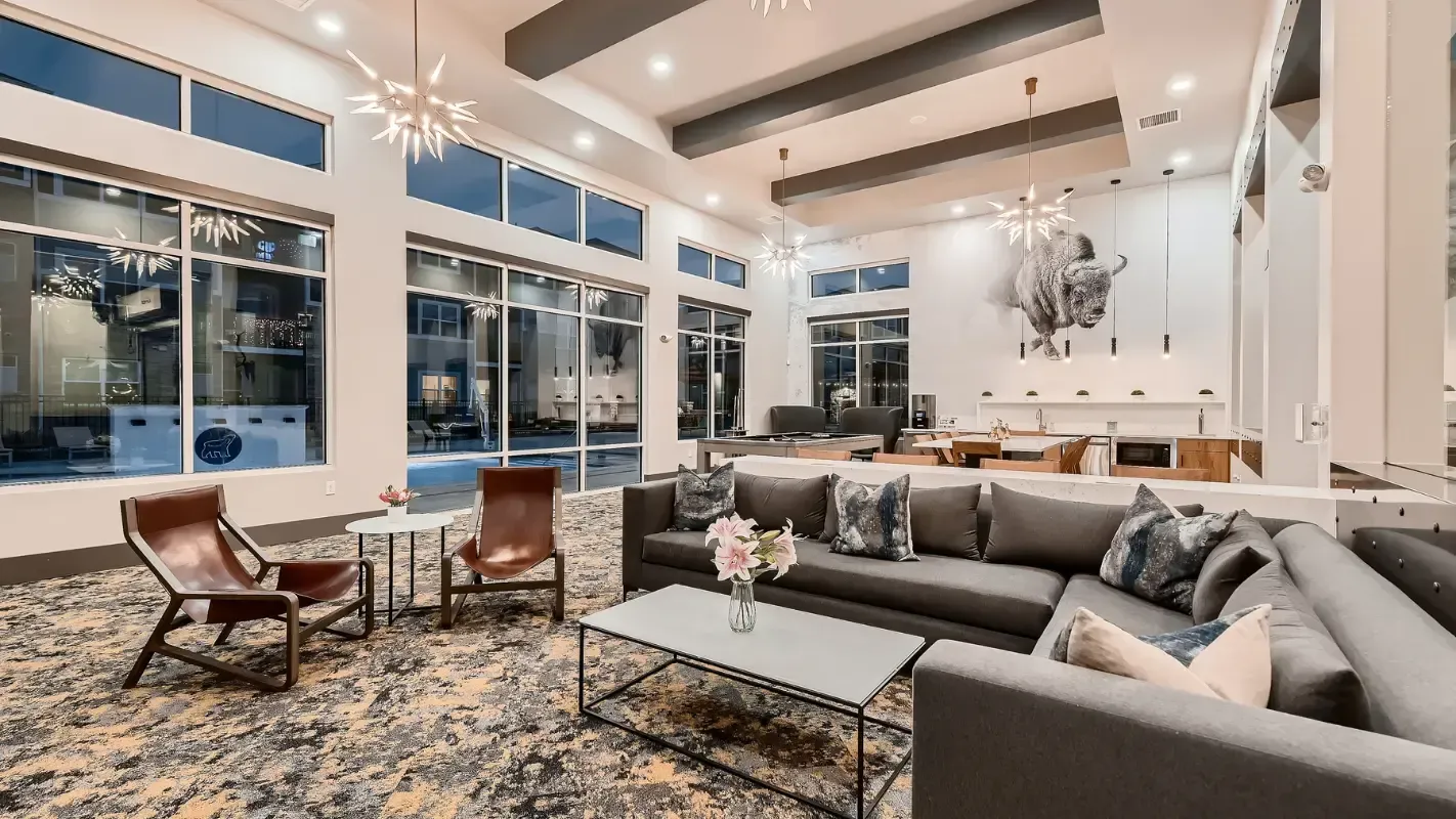 Spacious modern amenity lounge with a sectional sofa, chairs, and a kitchenette.
