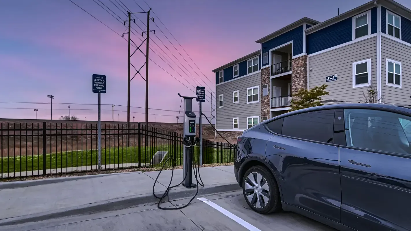 Electric car charging at a station near an apartment building, dusk setting.