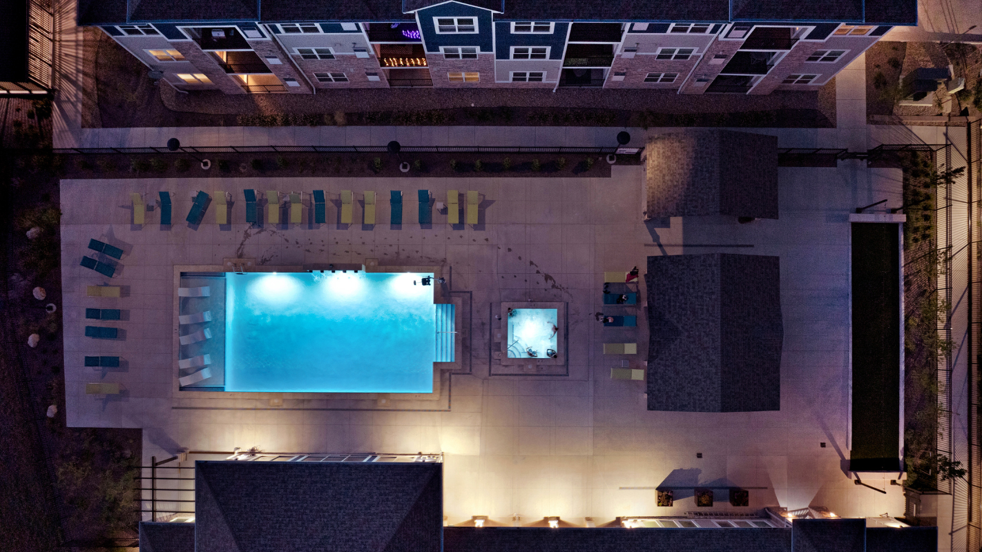 Aerial night view of a residential pool courtyard with lounge chairs.