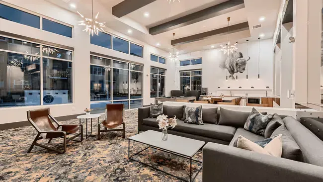 A modern lounge area with large windows, sectional sofa, armchairs, and a coffee table, with starburst light fixtures.