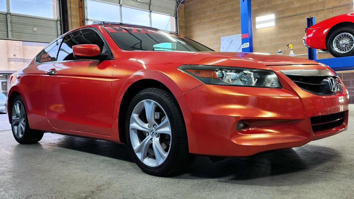 Red coupe sports car in an indoor garage, front-left view, metallic orange-red paint