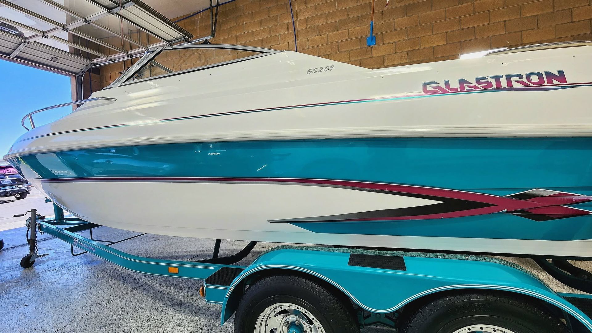 White speedboat named “Gladiator” on a teal trailer inside a garage or warehouse.