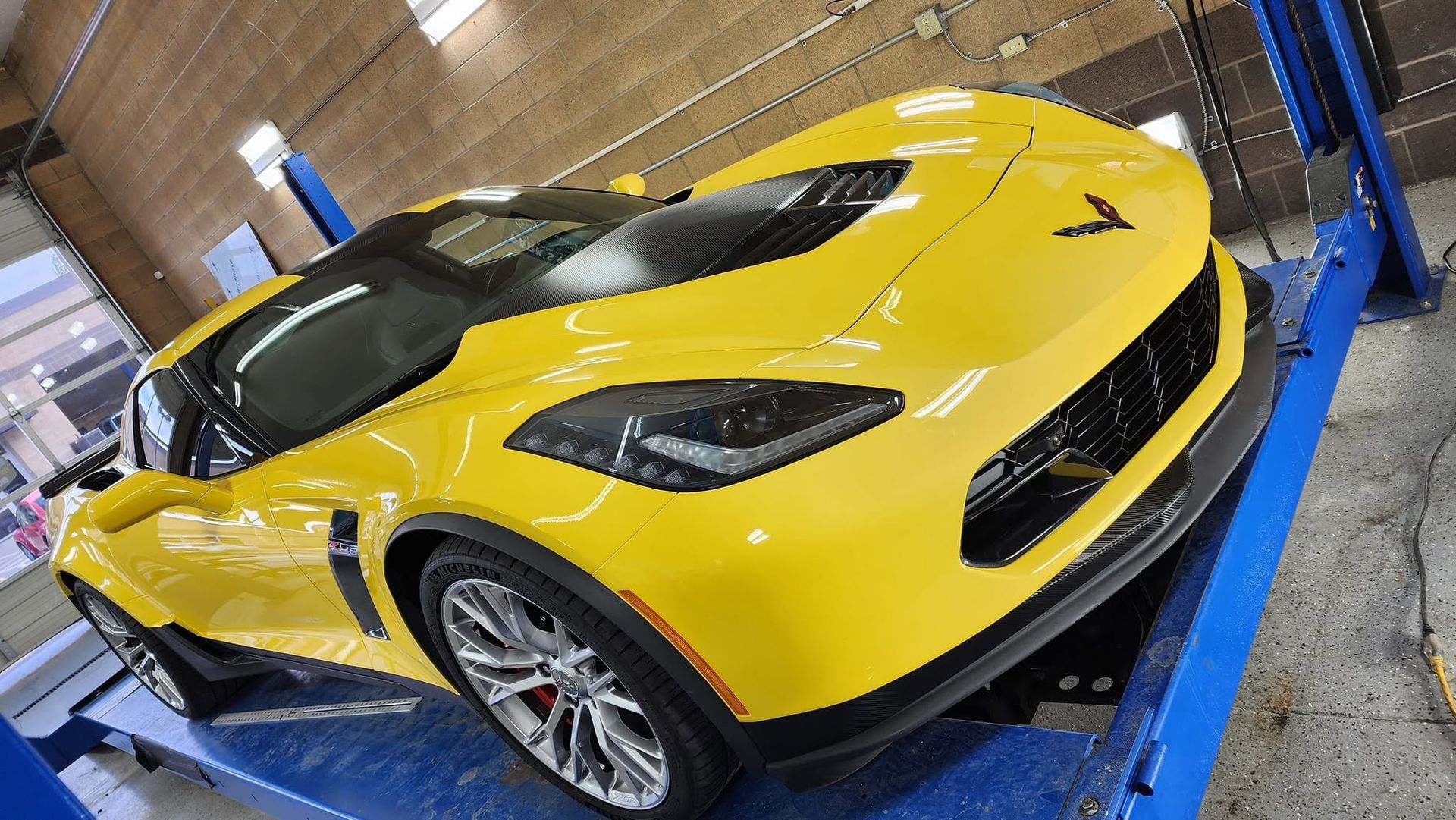 Yellow sports car on a blue lift inside a garage, viewed from the front-left side