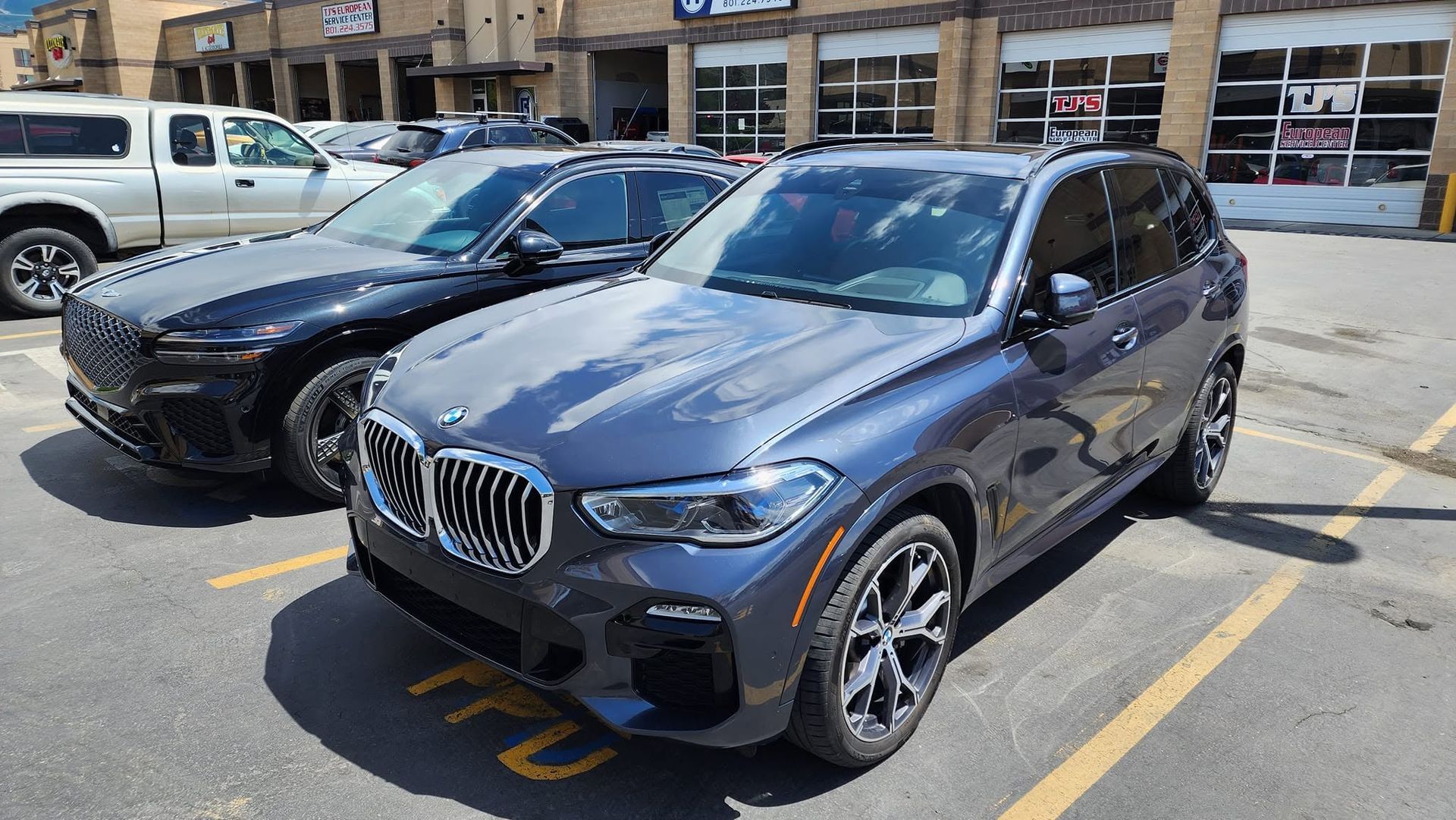 Two parked BMW SUVs in a parking lot, front gray car in foreground