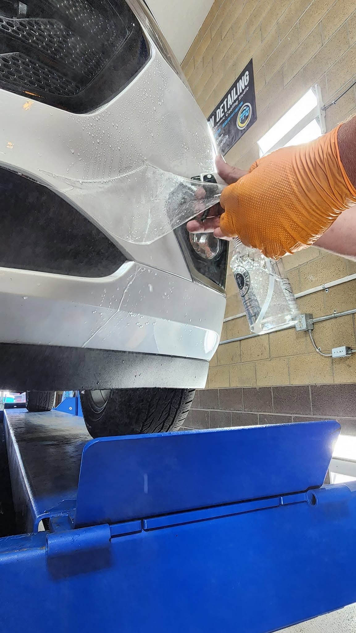 Hand spraying water onto a large silver wheel rim during cleaning, with a blue bin below.