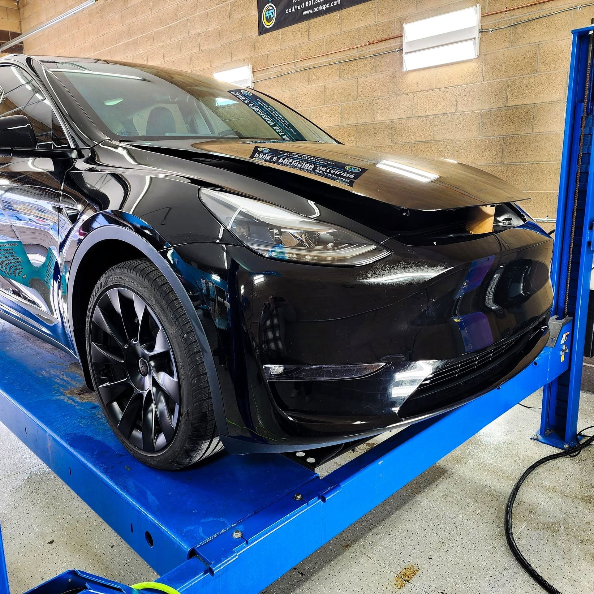 Black Tesla SUV on a blue lift inside a garage, with its front end partially raised for service