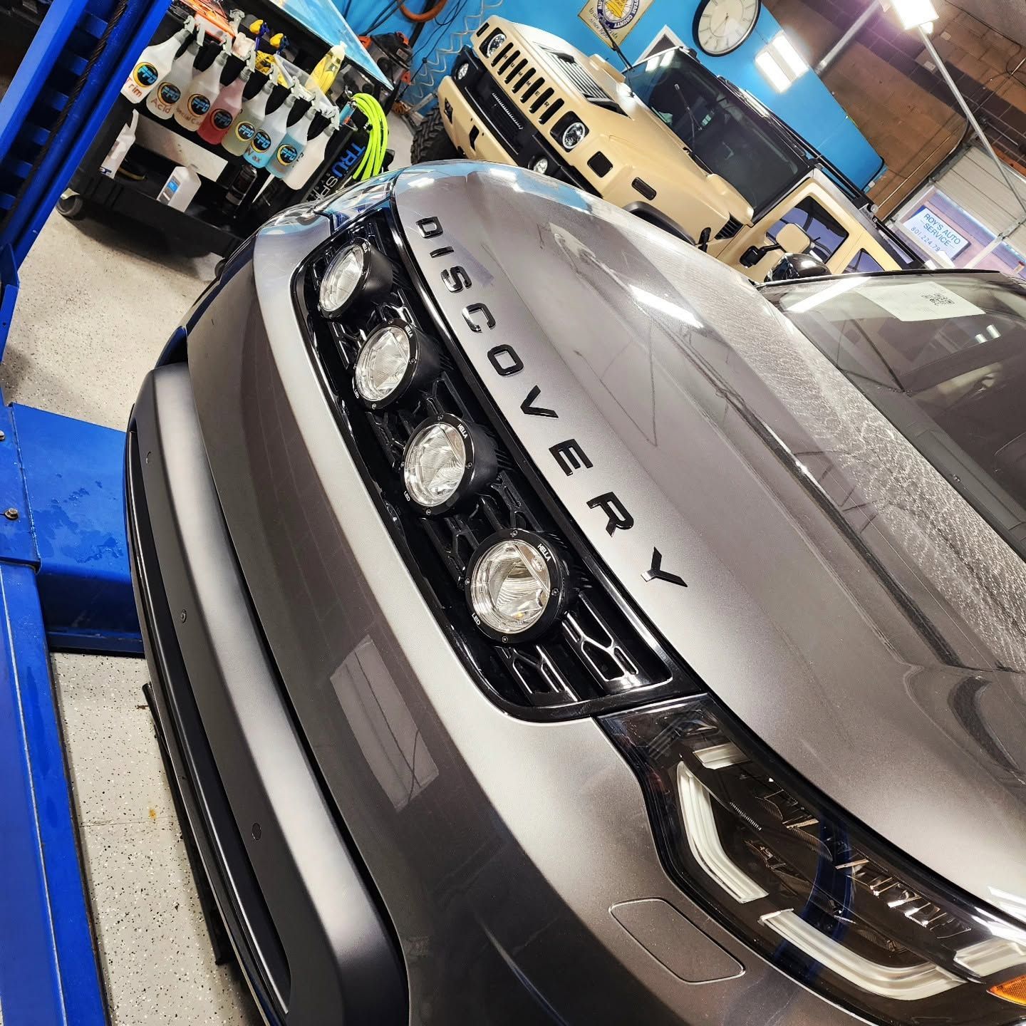 Close-up of a silver Land Rover Discovery in a garage, showing the grille and headlights.