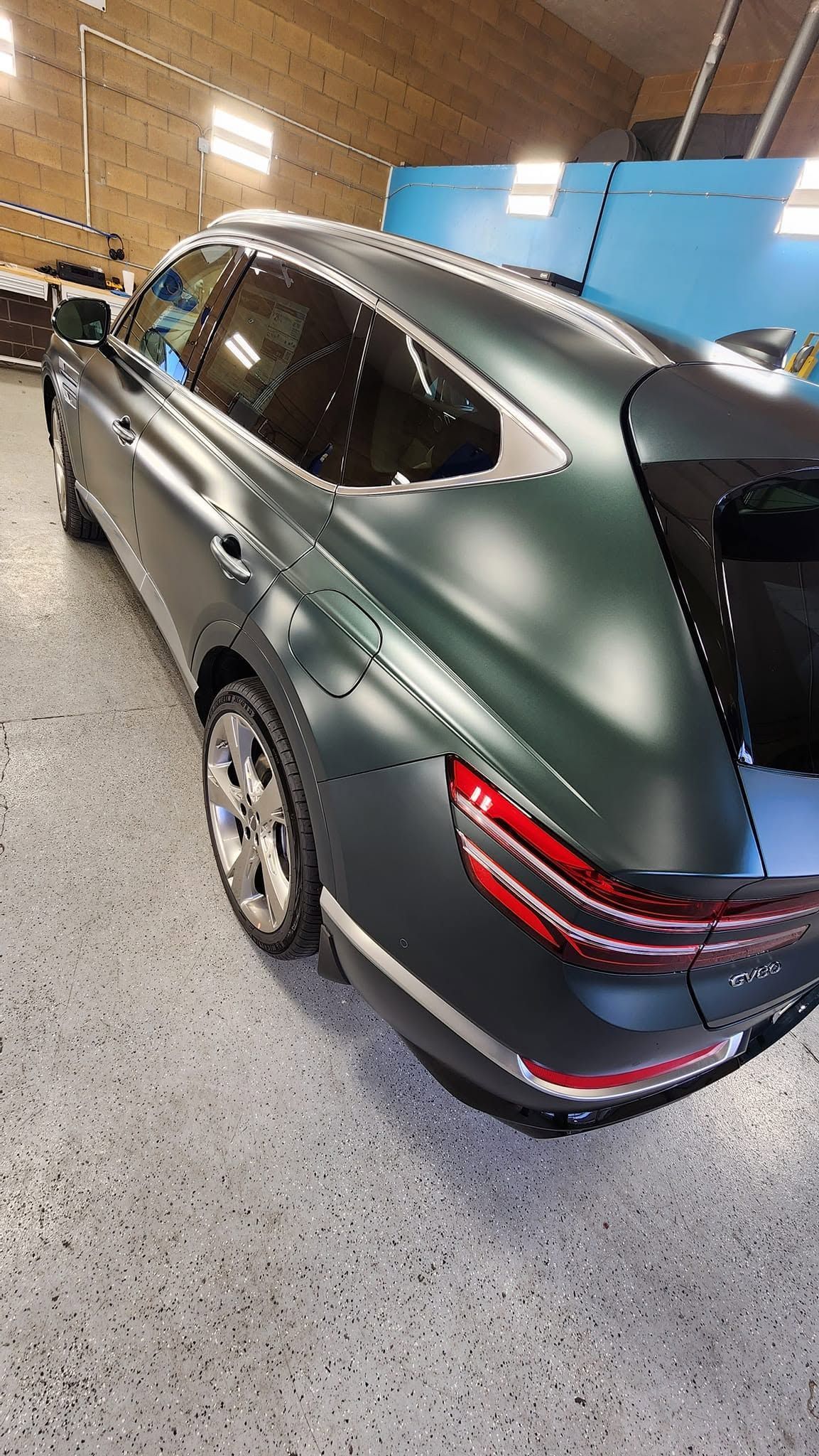 Dark green SUV parked indoors, rear three-quarter view on a speckled garage floor.