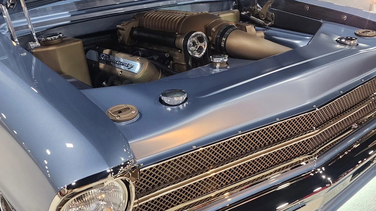 Close-up of a blue custom car engine bay with exposed chrome and tan intake pipes