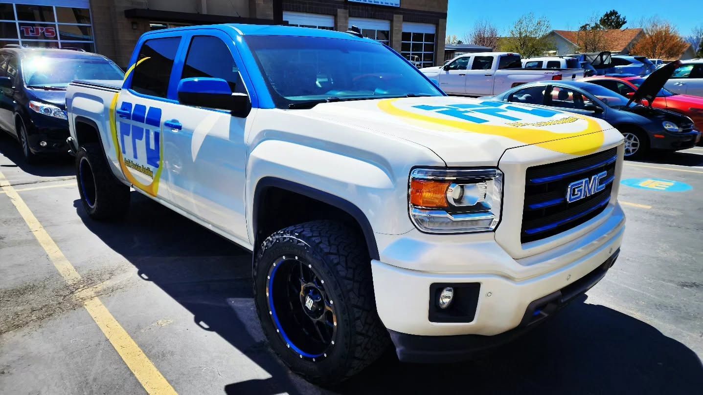 White GMC pickup truck with blue and yellow racing graphics parked outside a building