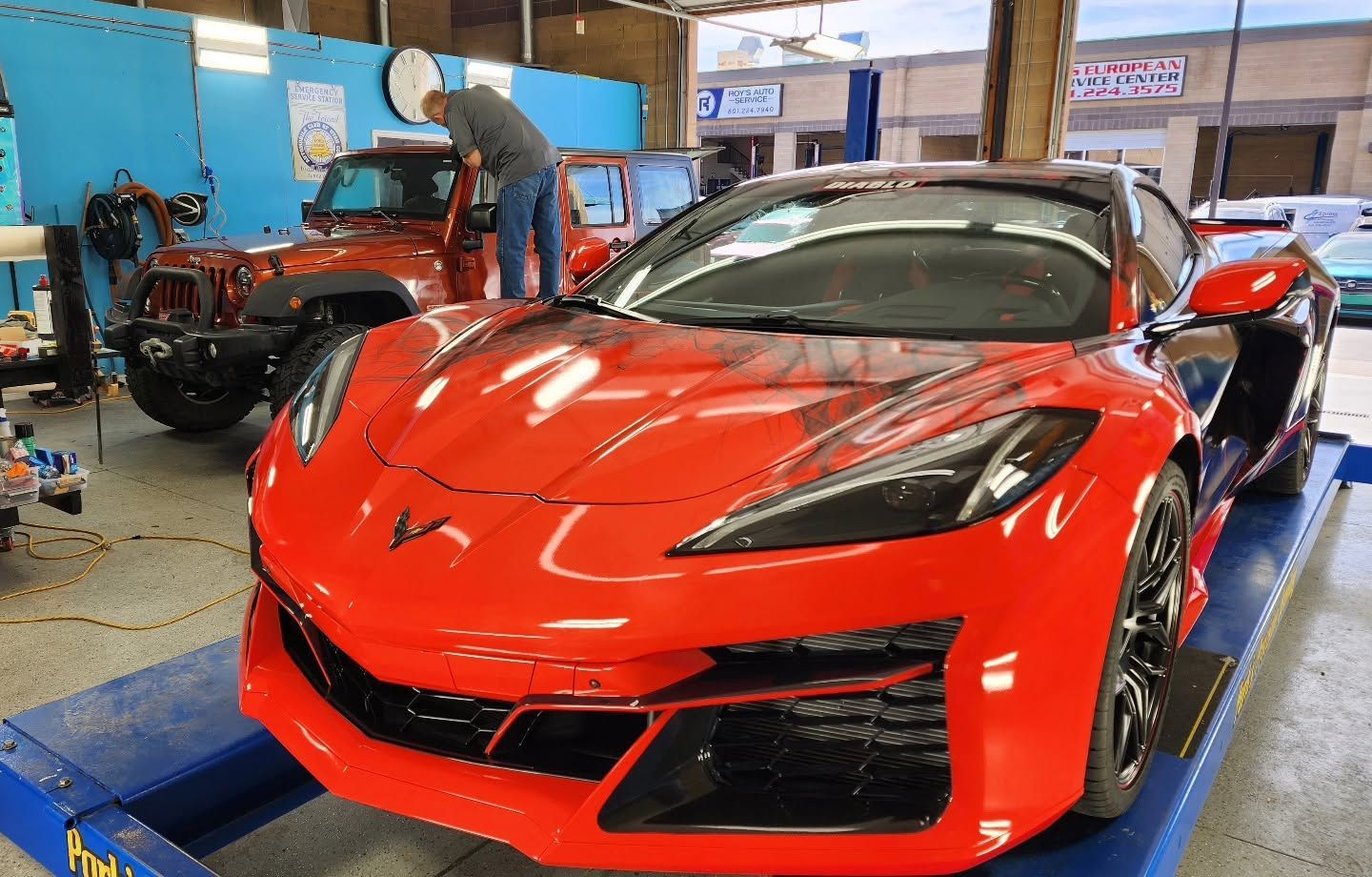 Red sports car in a workshop with a person working nearby on a lift