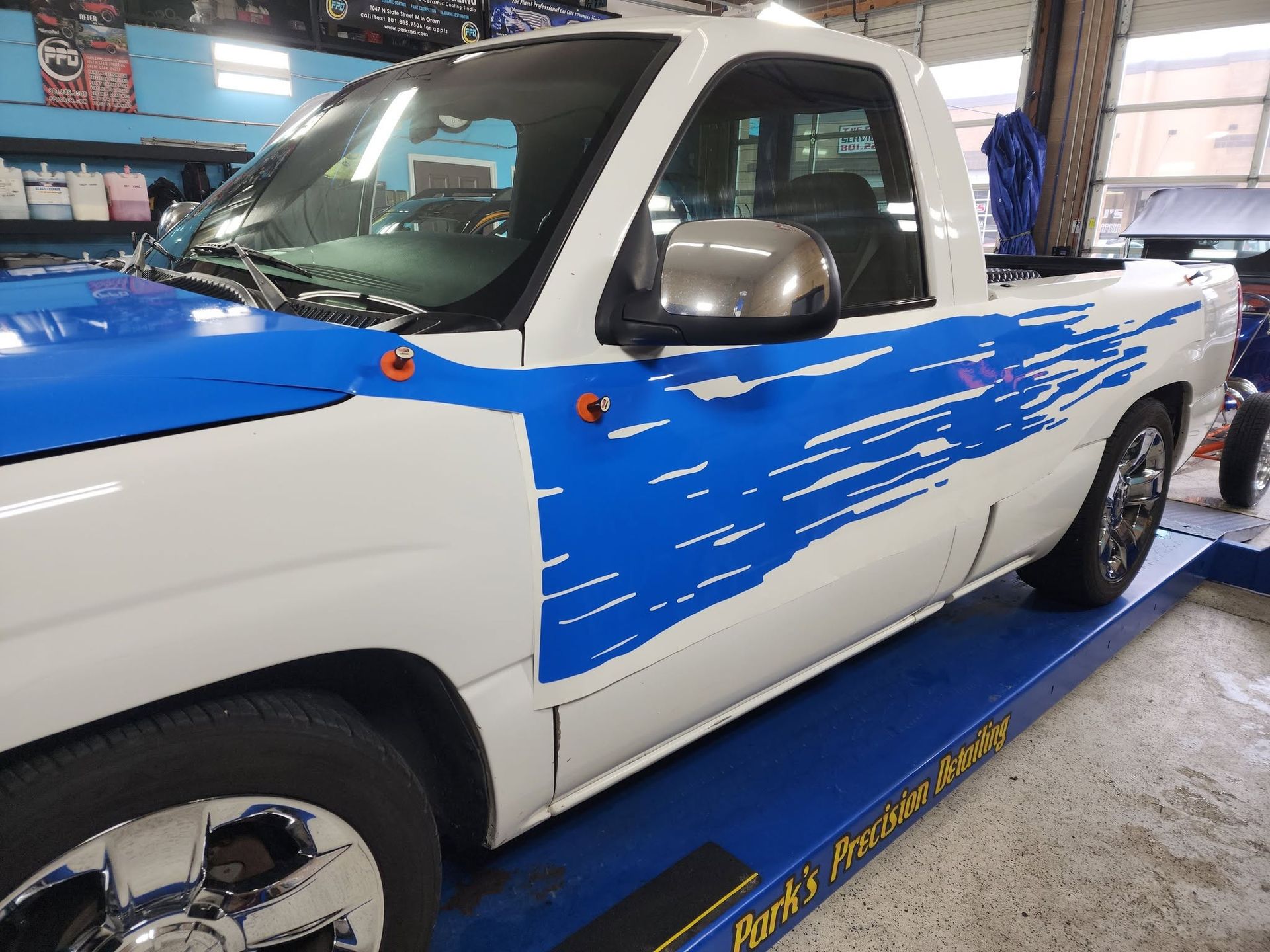 White pickup truck with blue paint-swipe graphics parked on a service bay lift
