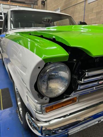 Front-left view of a classic car with bright green hood, white sides, and exposed front end in a garage