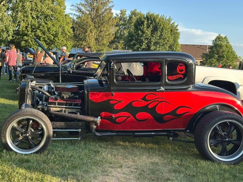 Red custom hot rod with flame decals parked on grass outdoors, side view