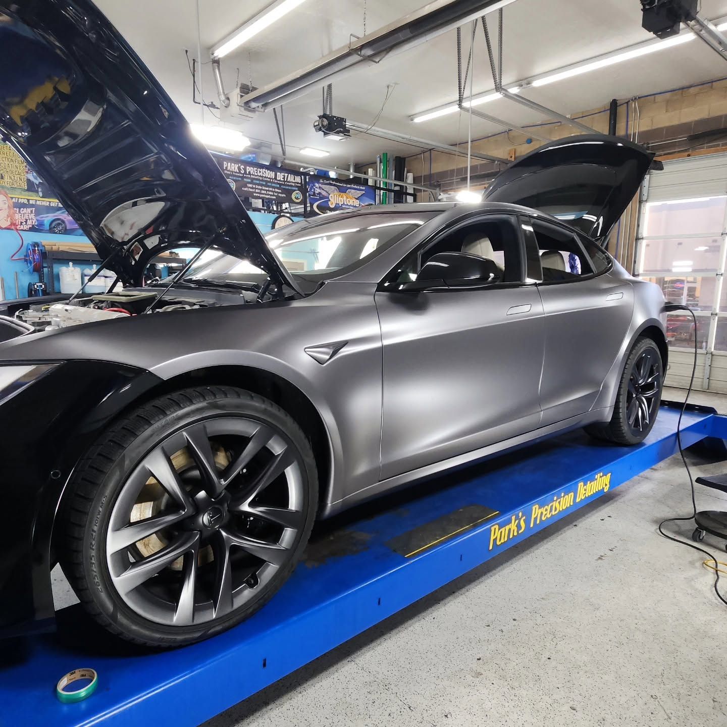 Gray sports car on a blue lift in an auto repair shop, hood open for service