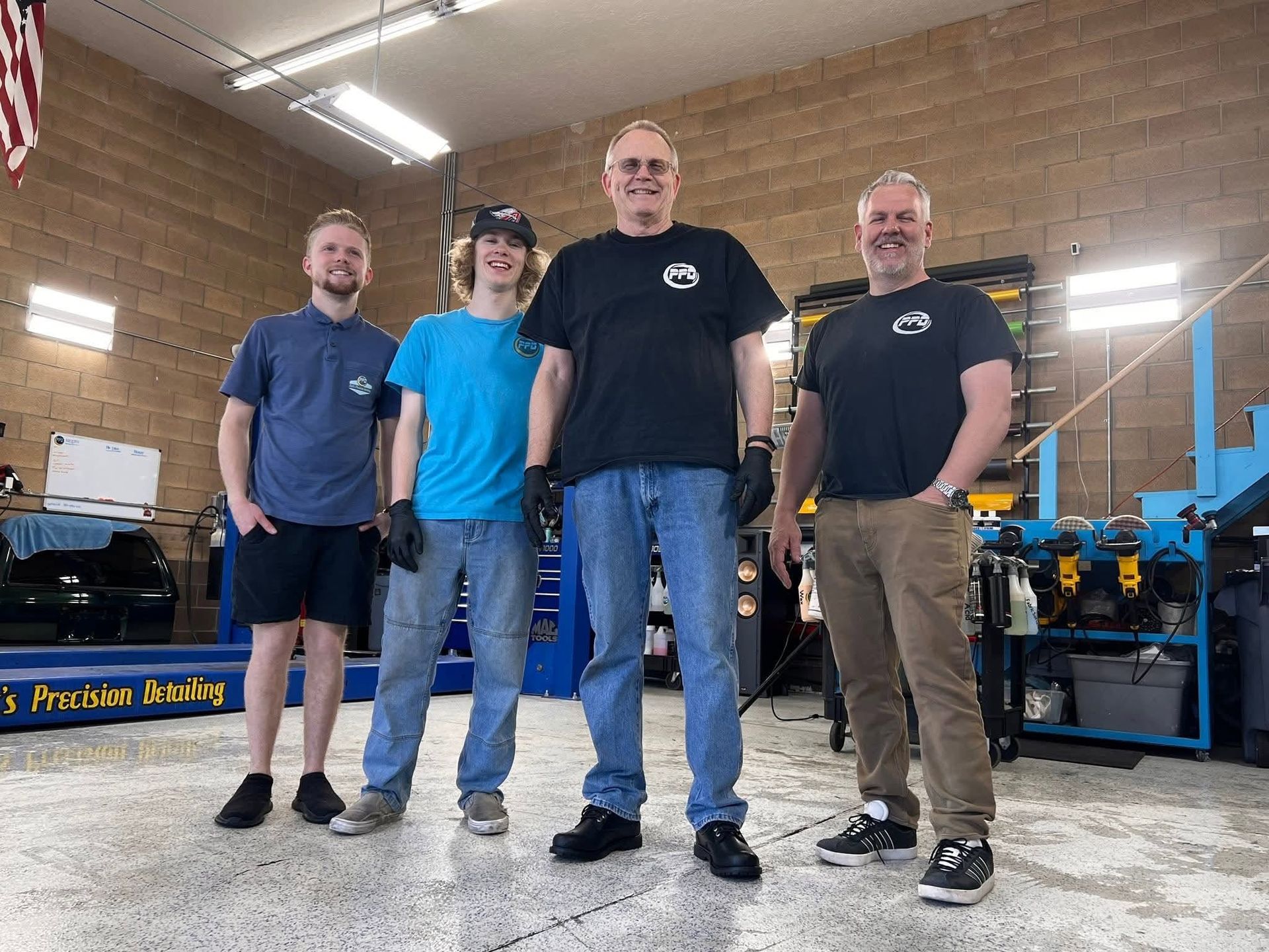 Four people standing in a workshop beside blue industrial machinery, smiling at the camera