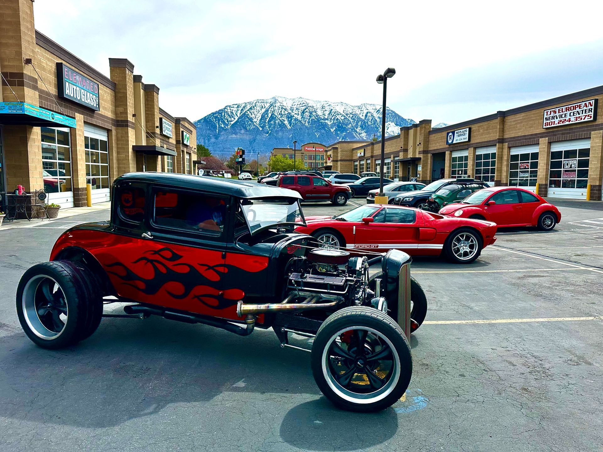 Custom red-and-black hot rod parked in a shopping center lot with snowy mountains in the background