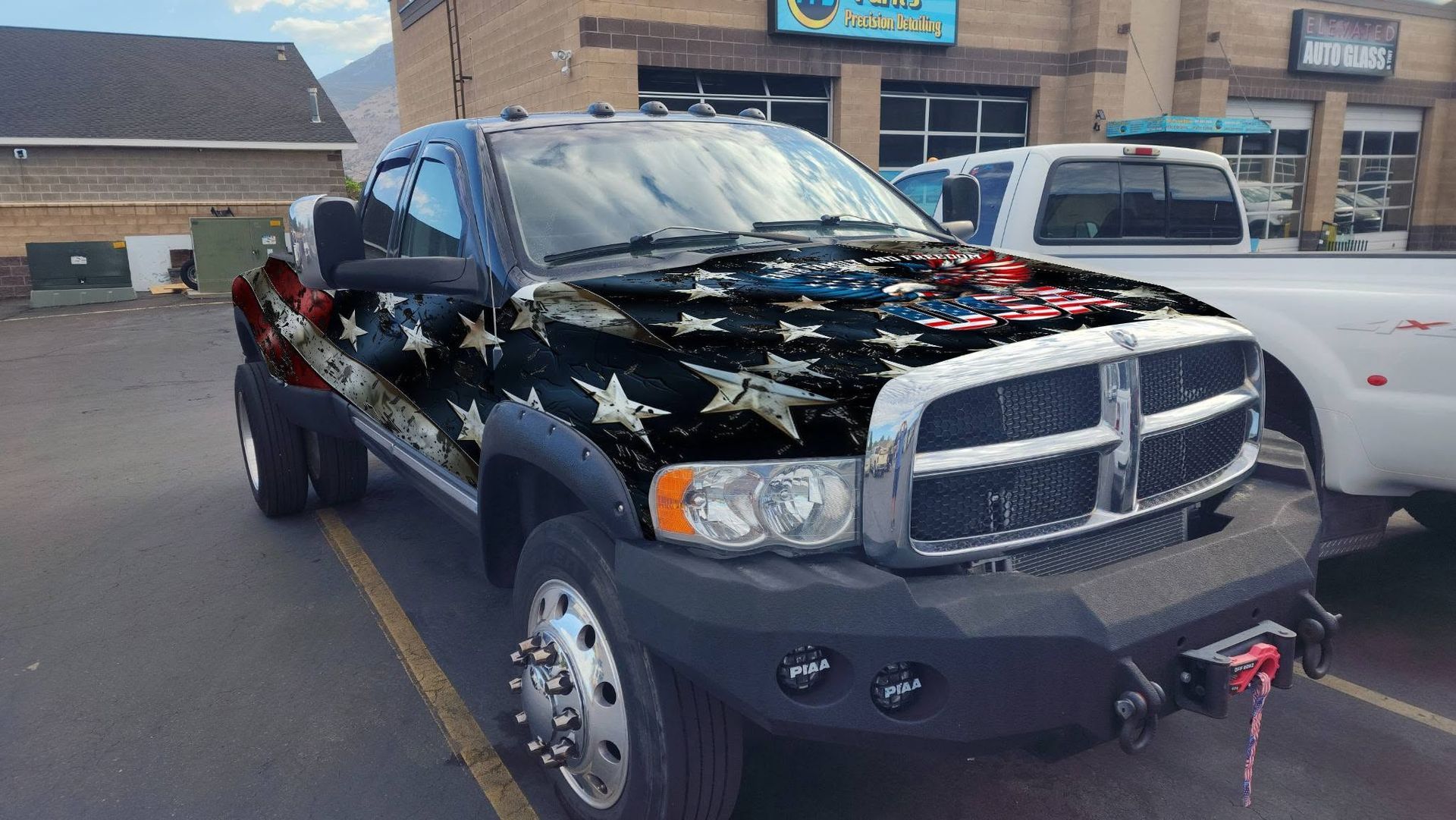 Black pickup truck with an American flag paint design parked in a lot near a storefront.
