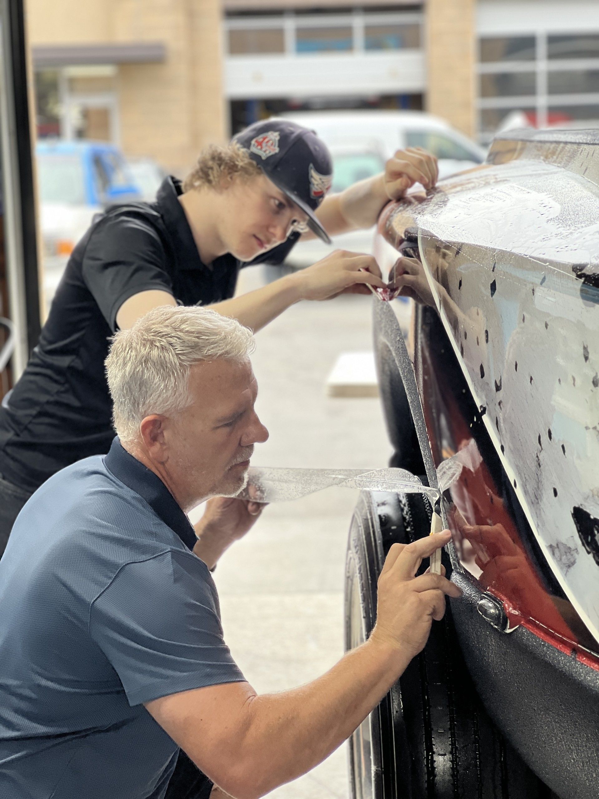 Two people polishing a black car’s rear bumper in a workshop