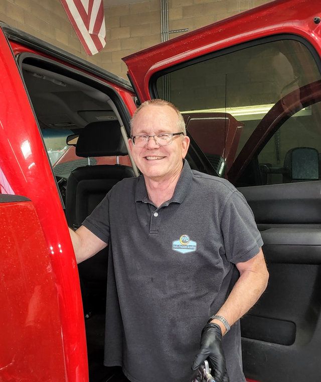 Smiling mechanic in gloves standing by open red vehicle door in a garage