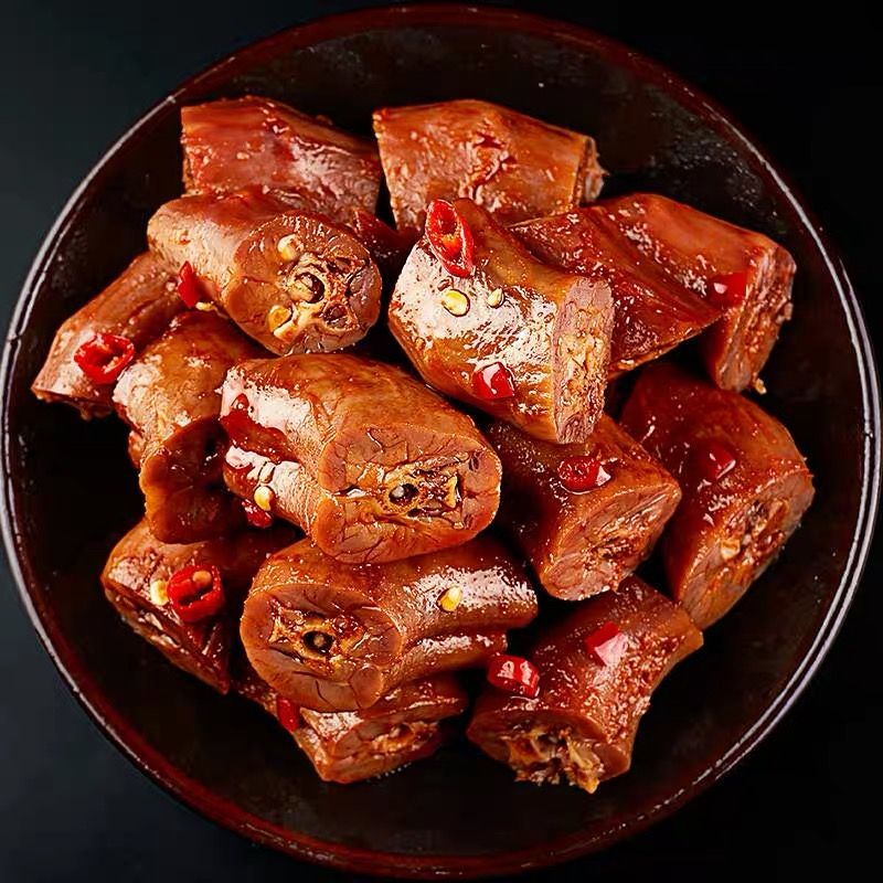 Bowl of glazed braised meat chunks with red chili peppers on a dark background