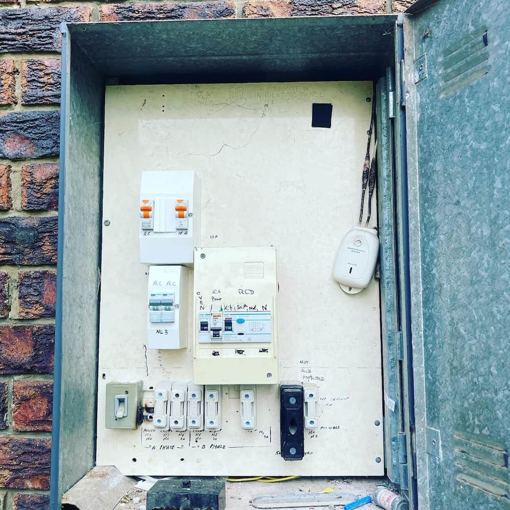 A Brick Wall with A Metal Box Filled with Electrical Equipment — Higgins Electrical in Aura, QLD