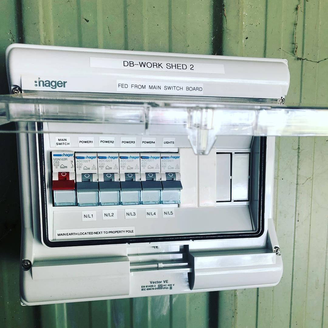 A White Electrical Box Is Hanging on A Green Wall — Higgins Electrical in Landsborough, QLD