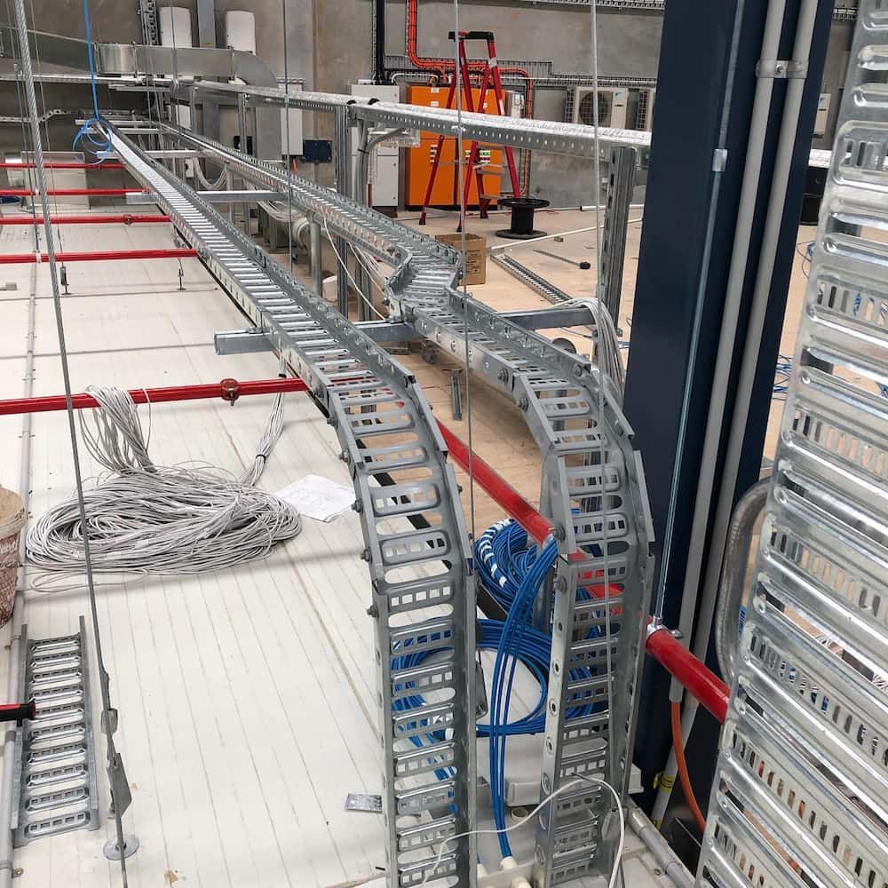 Cable trays installed overhead in a large room. Wires and pipes run alongside them — Higgins Electrical in Aura, QLD