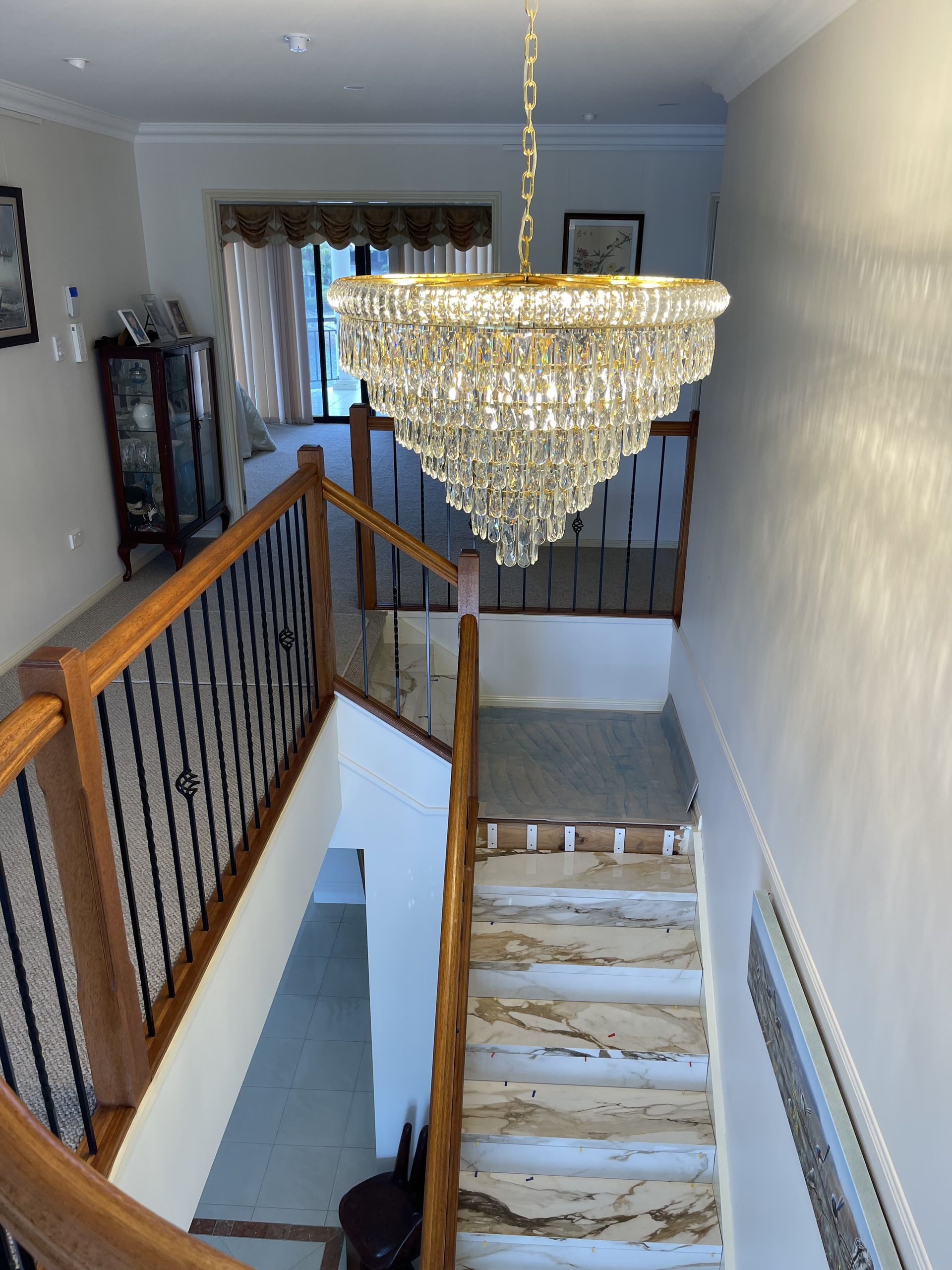 Chandelier Hangs Above a Staircase With Wooden Railings — Higgins Electrical in Narangba, QLD