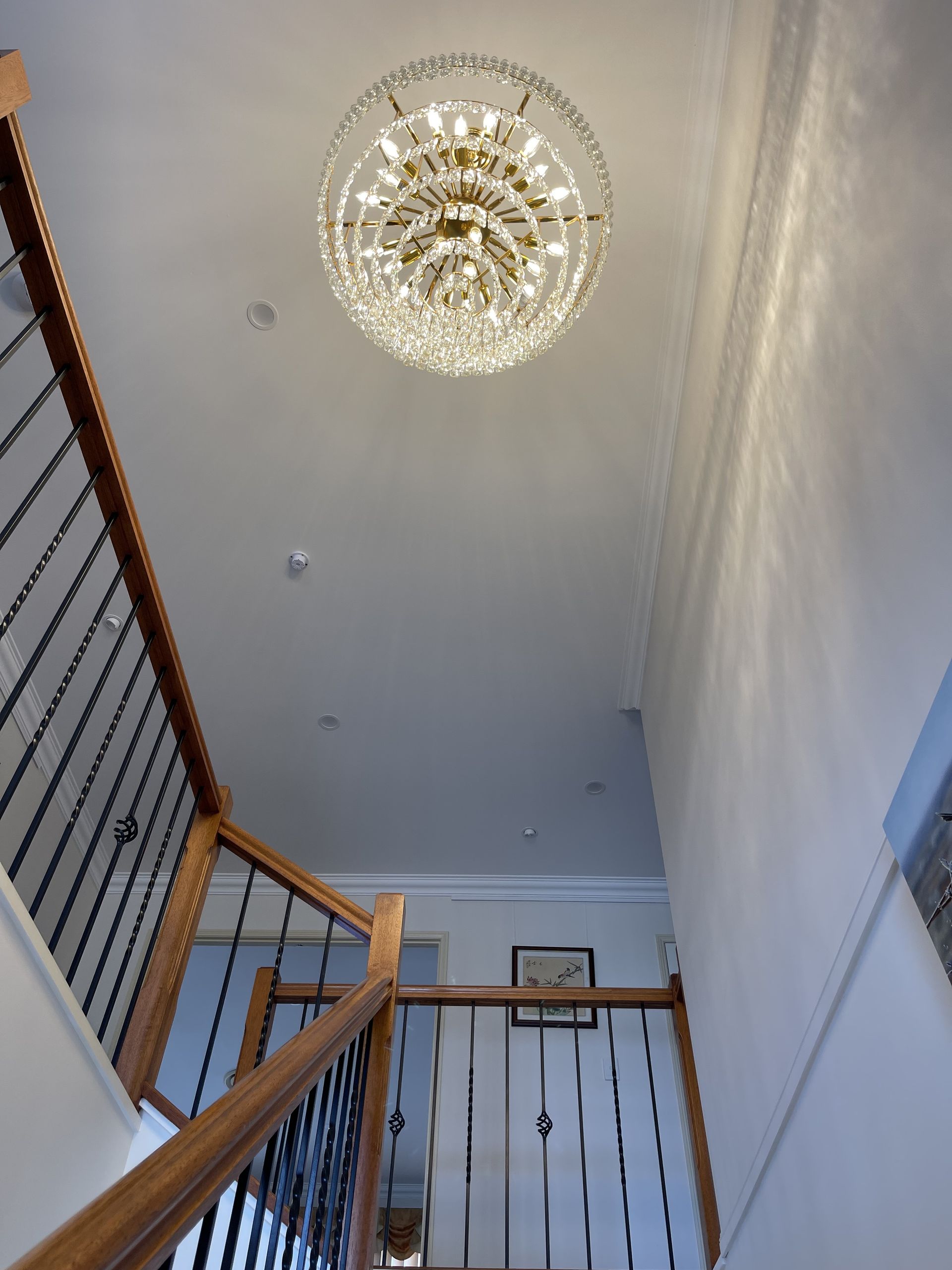 Grand Foyer: Chandelier Hangs Above Staircase With Wooden Railings and Black Spindles — Higgins Electrical in Caboolture, QLD