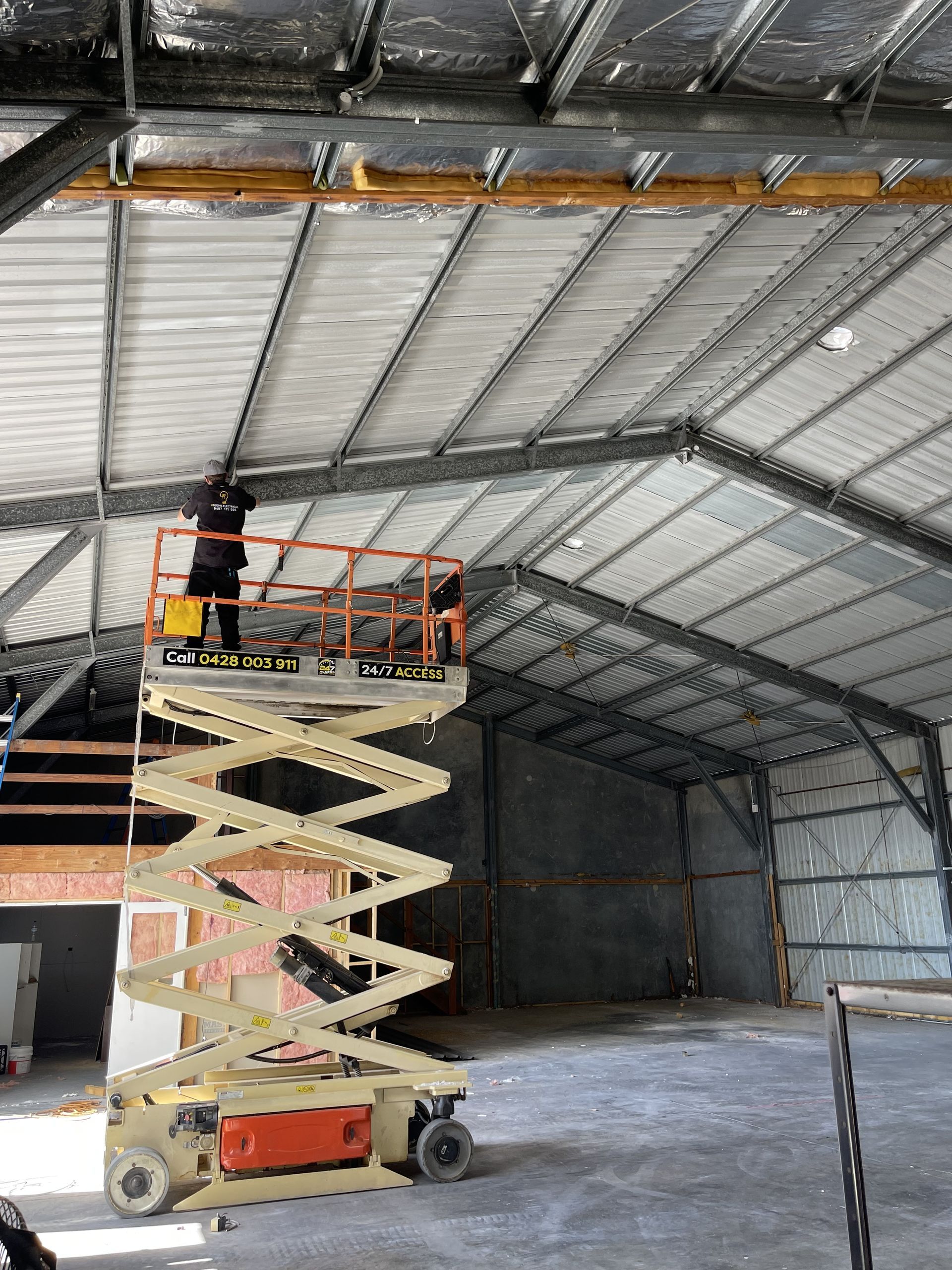 A Man Is Hanging a Light Fixture from The Ceiling — Higgins Electrical in Beerwah, QLD