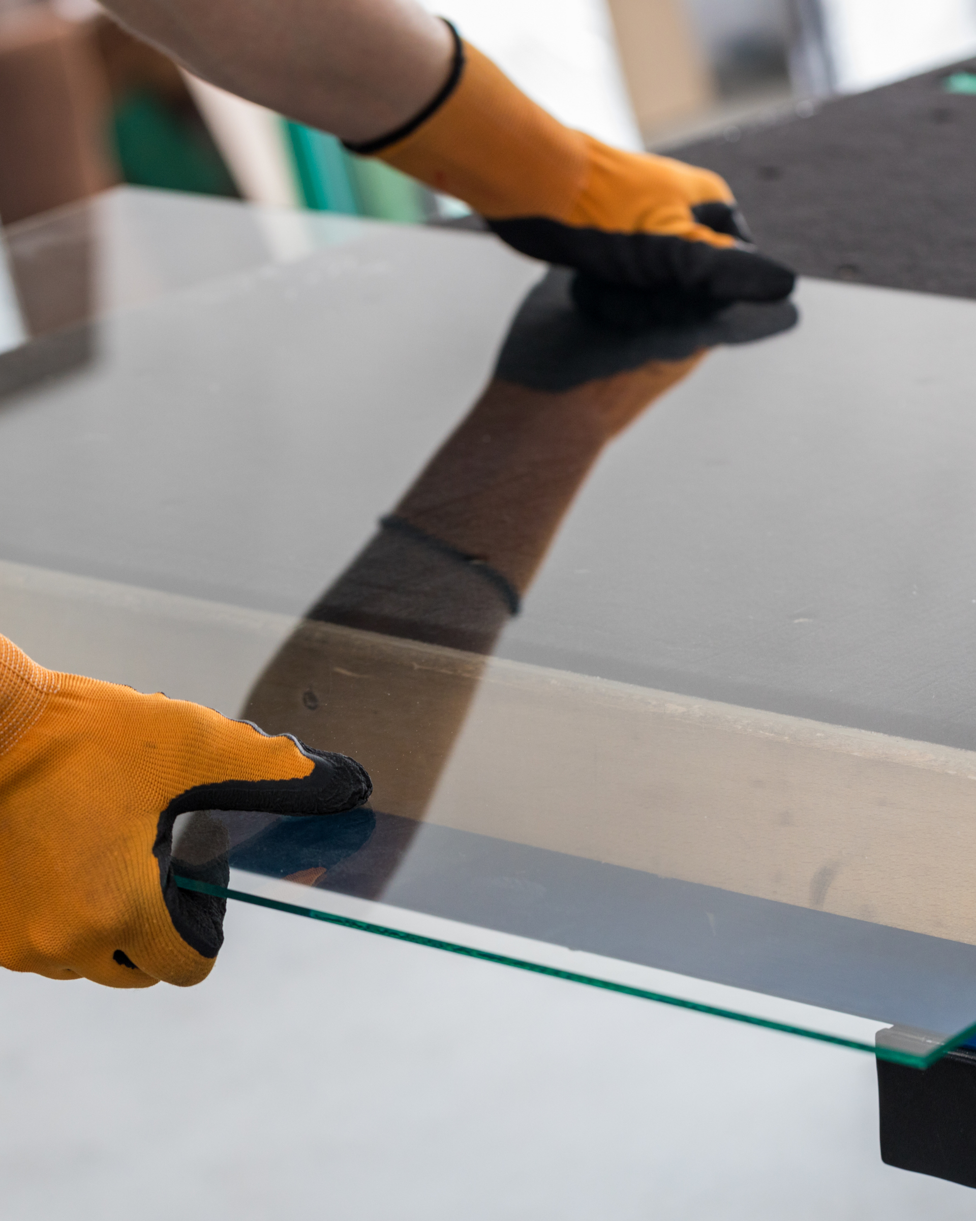 Gloved hands carefully positioning a large glass pane on a table