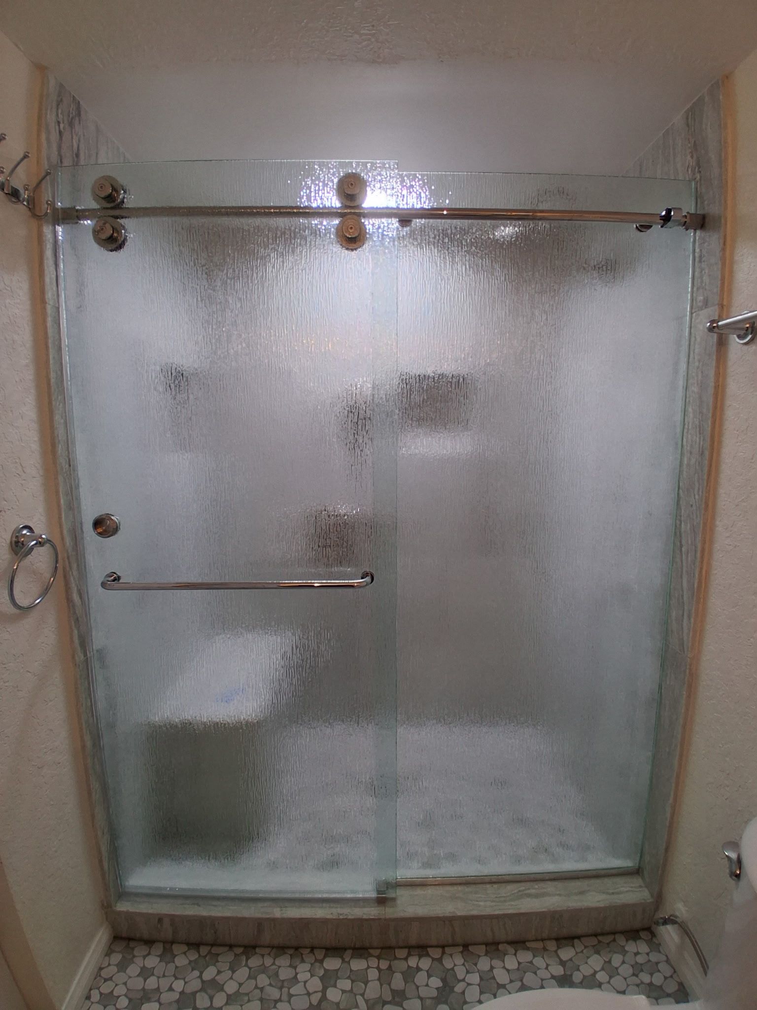 Glass shower enclosure with frosted doors and chrome handles in a bathroom