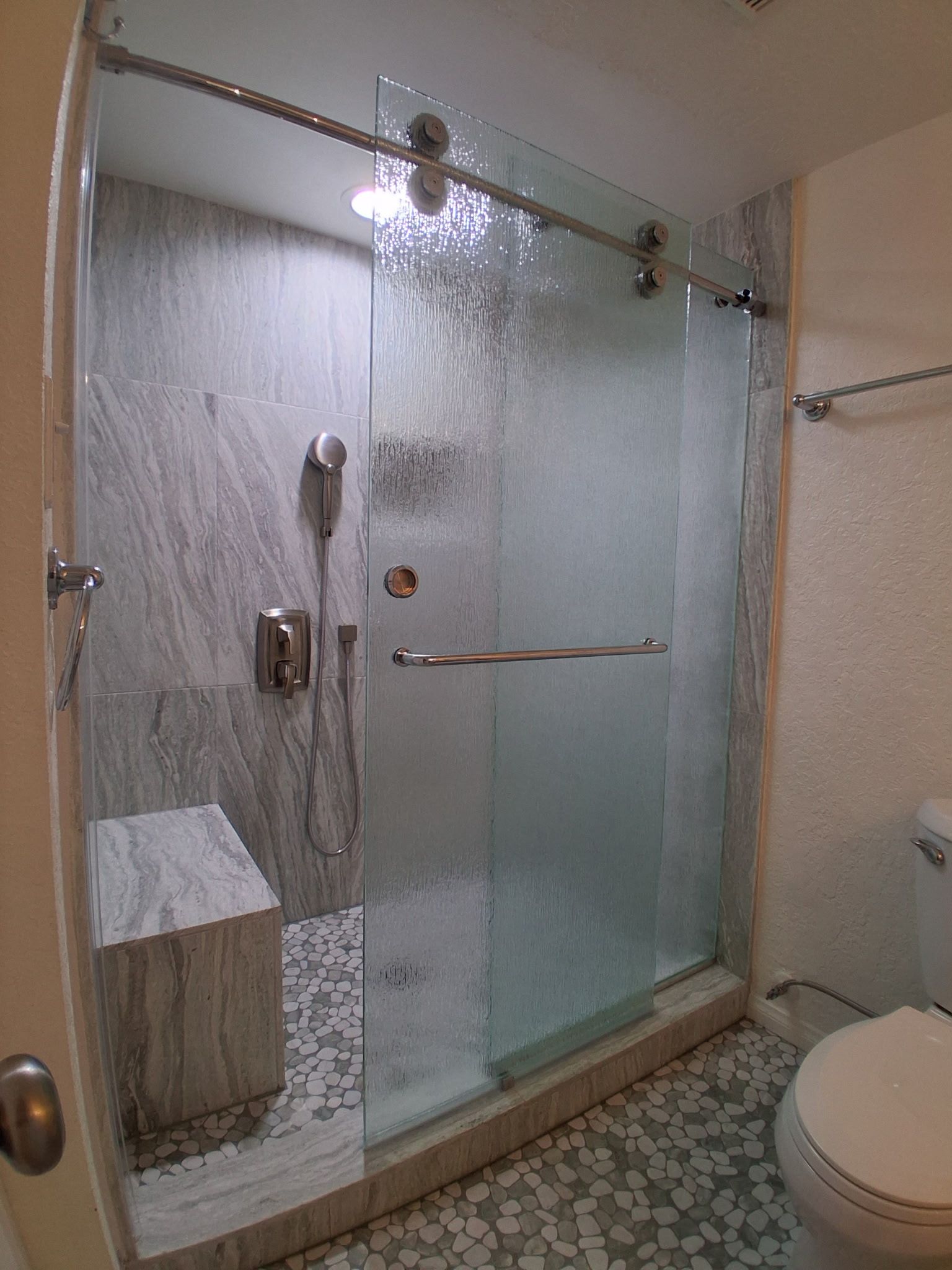 Glass walk-in shower with rain showerhead and handheld wand in a tiled bathroom