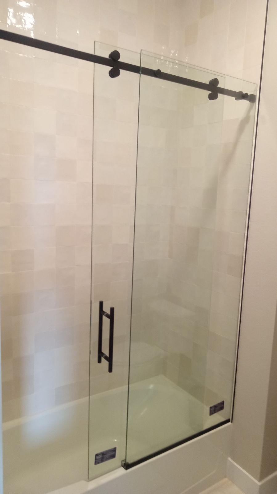 Glass sliding shower door with black hardware in a beige bathroom