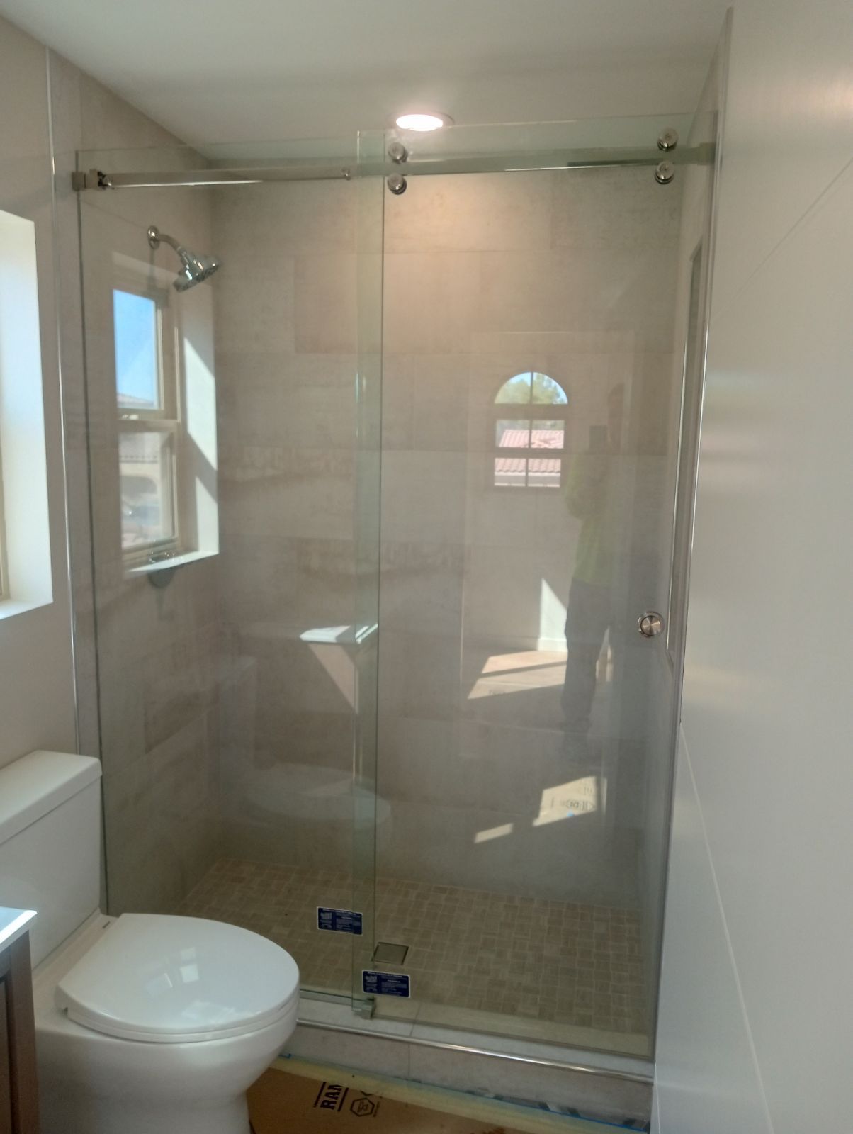 Bathroom with glass walk-in shower, toilet, and window light from the left.
