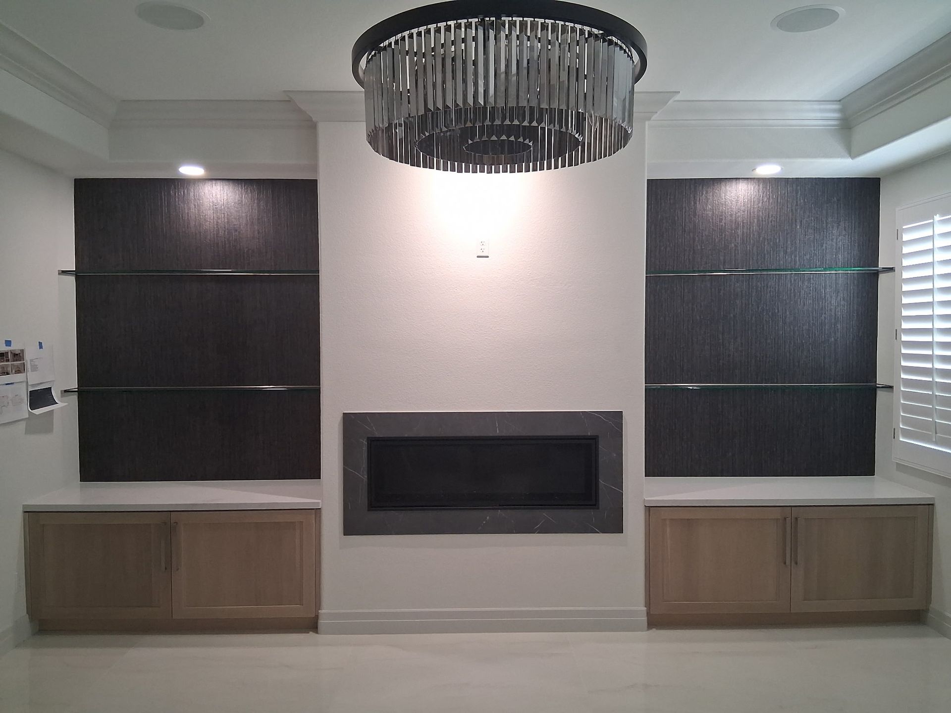 Modern living room wall with a central fireplace, dark built-ins, and a black chandelier