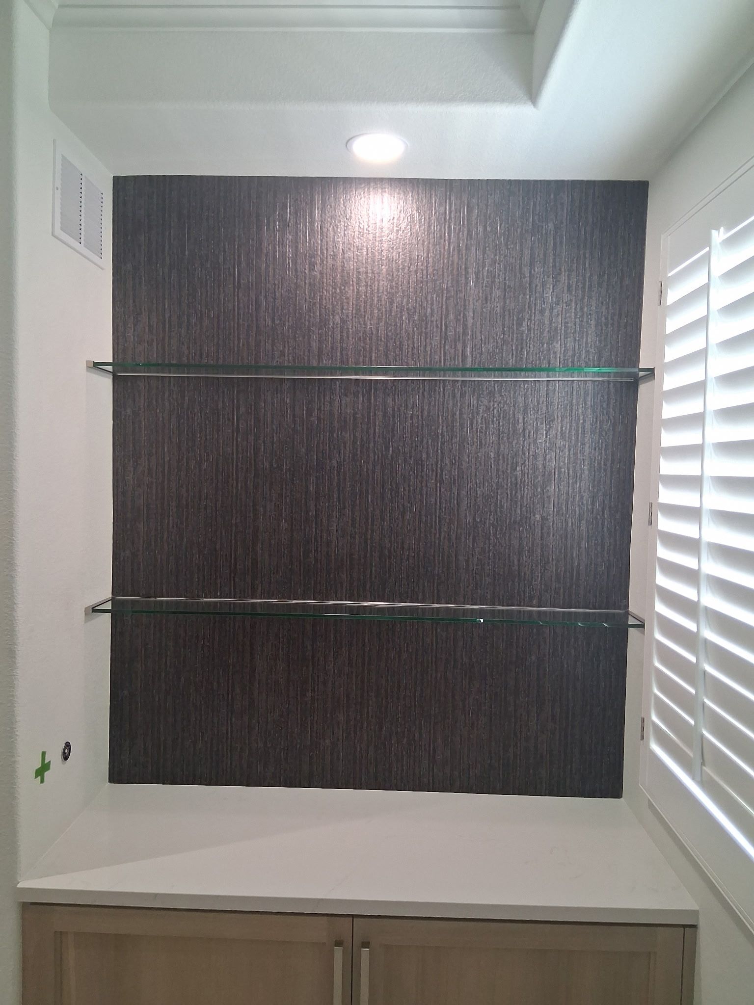 Bathroom shower with dark tiled wall, glass shelf, and white shutters