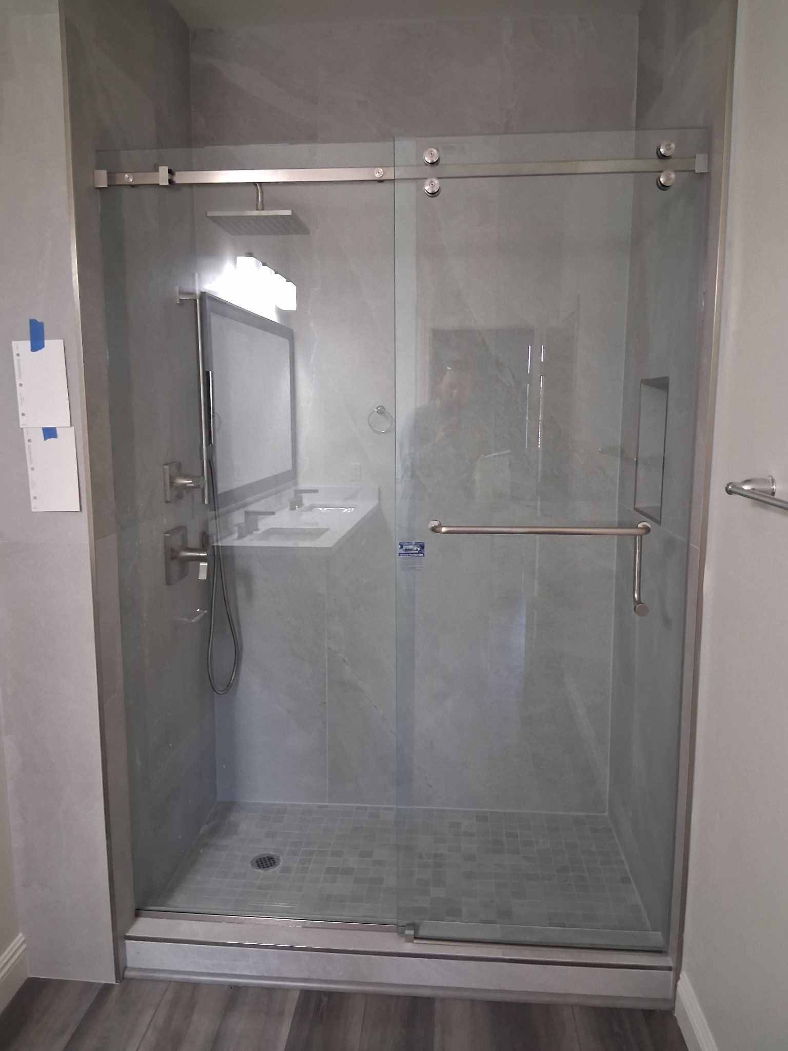 Glass shower enclosure with gray tile walls and a handheld shower head