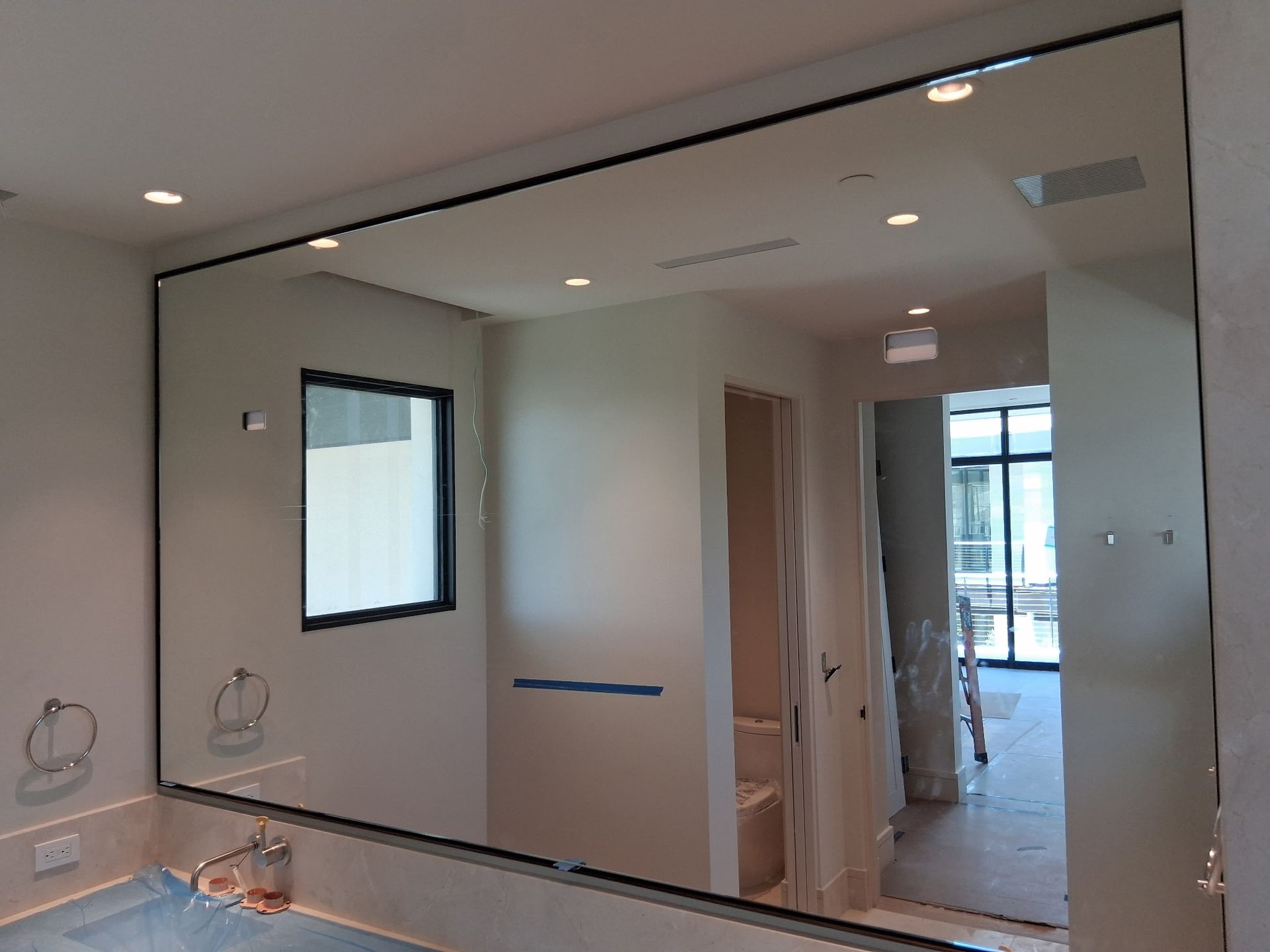 Partially tiled bathroom with large wall mirror, window, and unfinished cabinetry