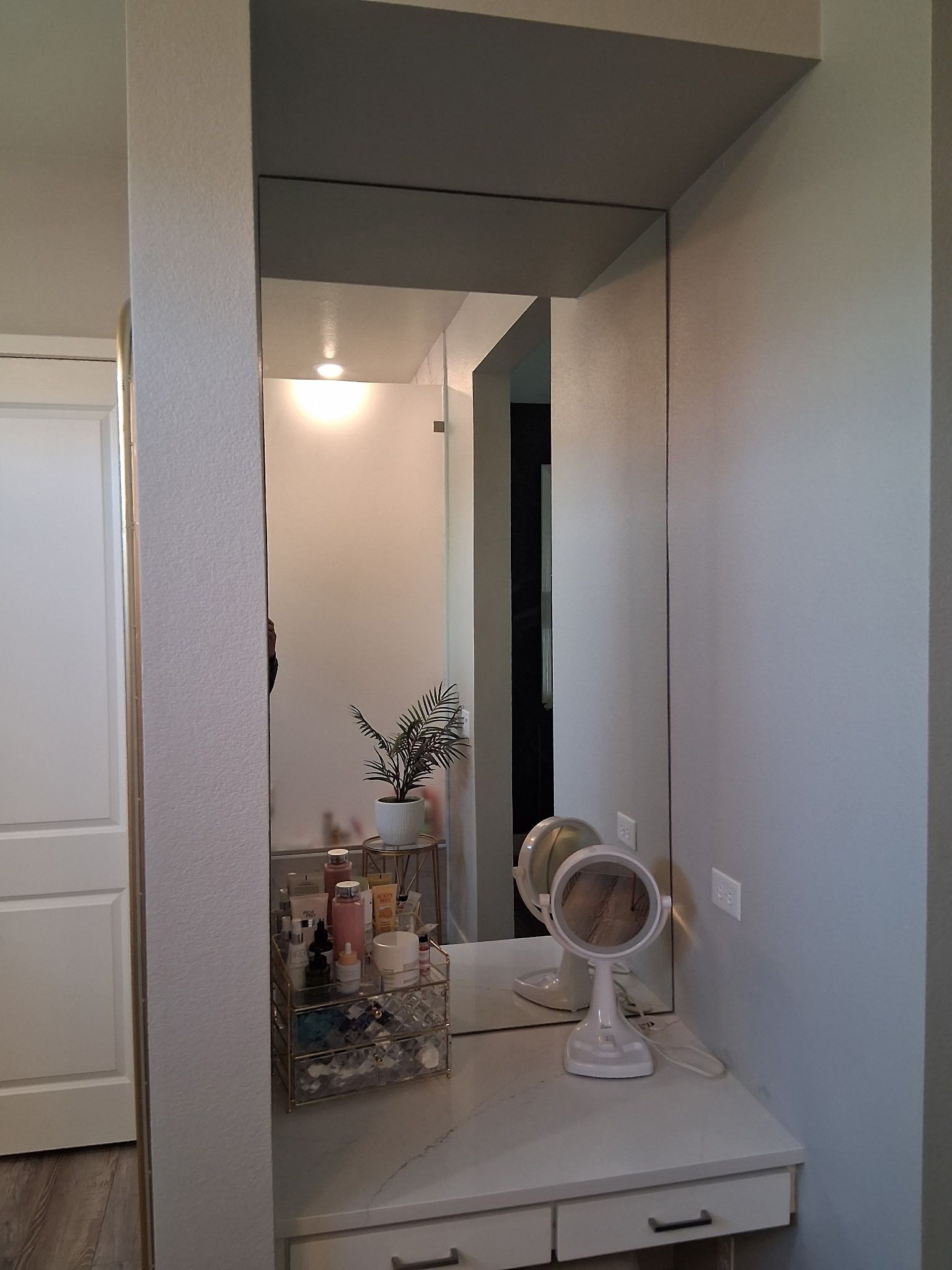 Narrow hallway vanity with mirror, lamp, flowers, and small fan on a white dresser, in a beige room