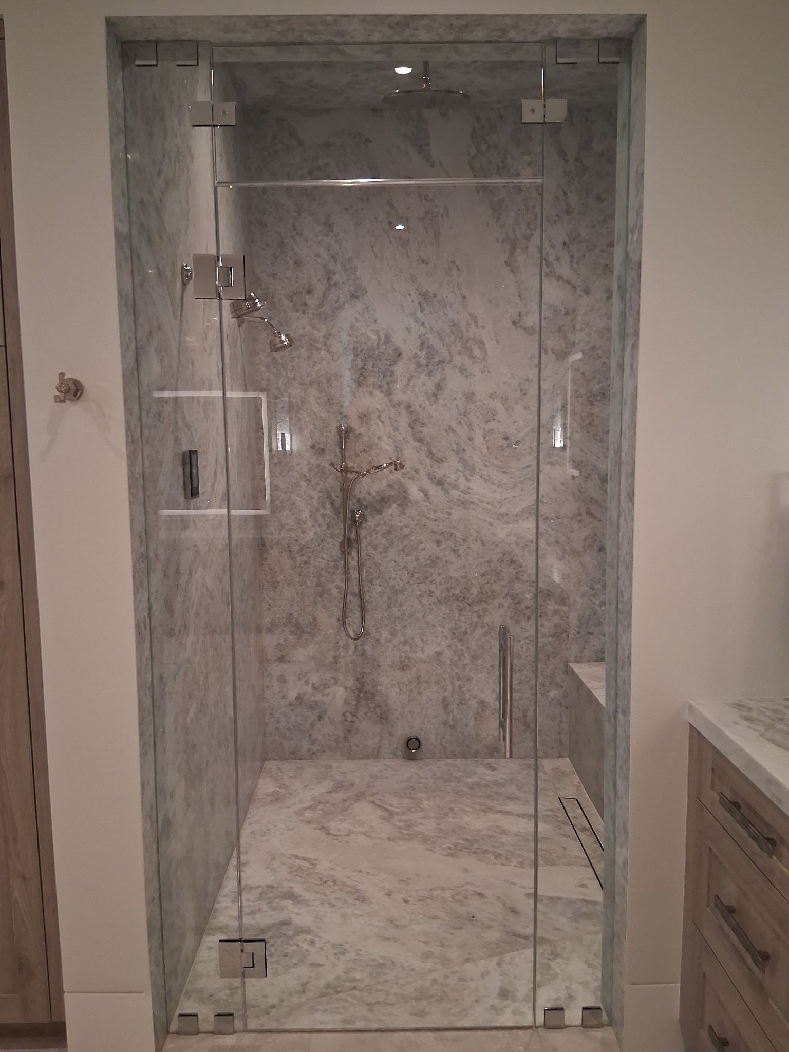 Glass walk-in shower with marble-look tile, built-in shelves, and a bench.