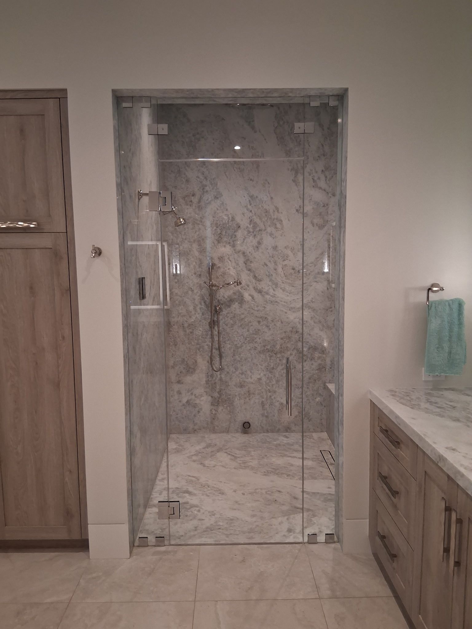 Bathroom with marble shower stall, wood vanity, and cabinet beside a glass shower door.