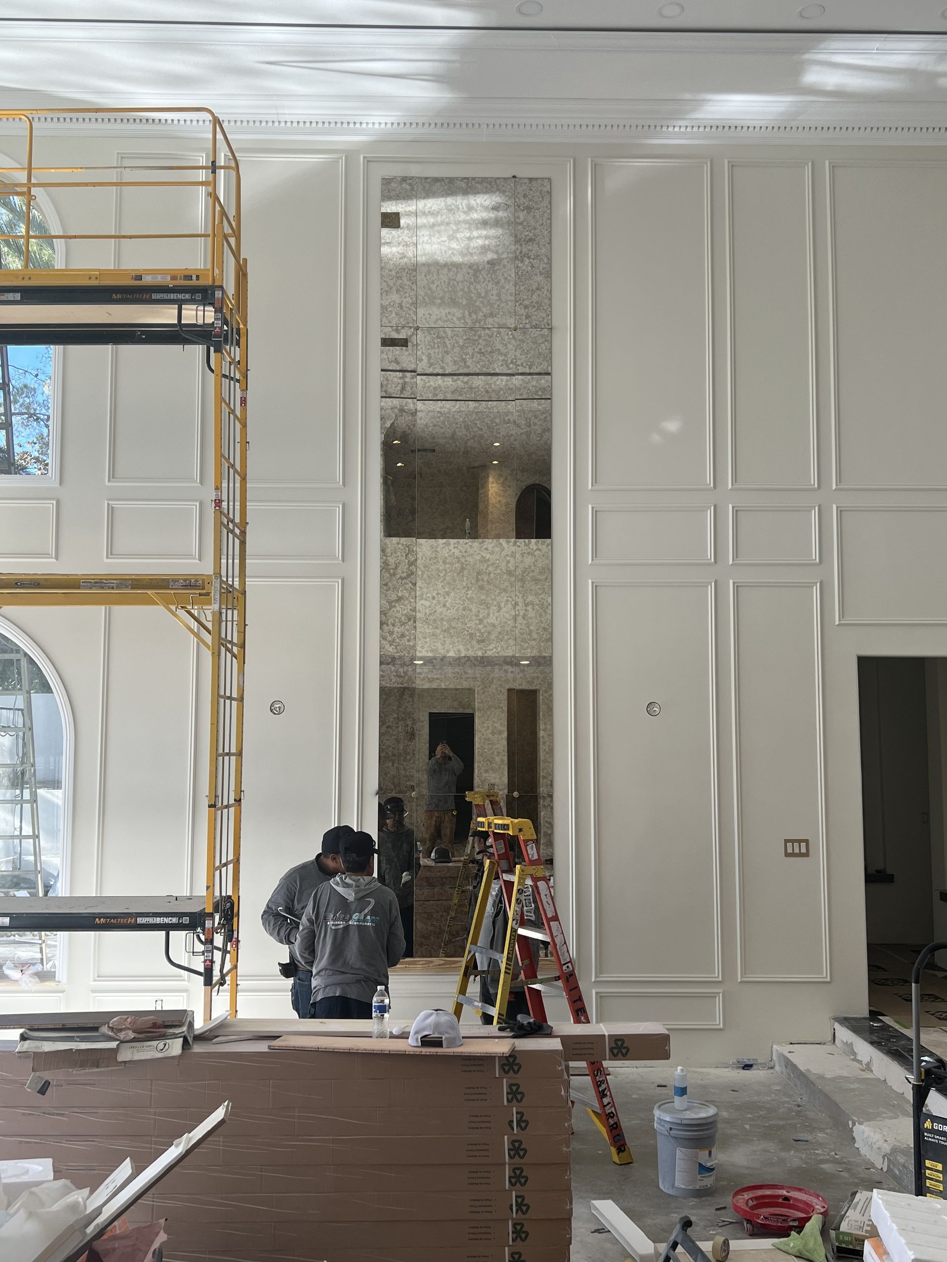 Person working on scaffolding inside a white-walled room with tall window and construction materials nearby