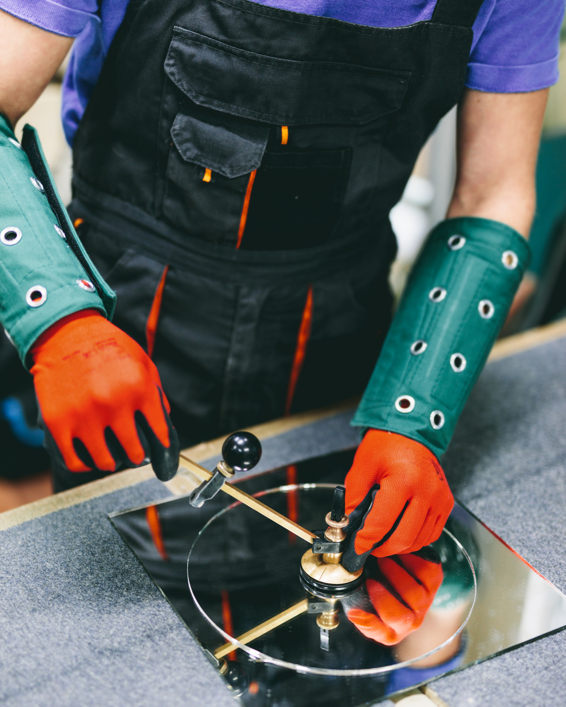 Person in safety gloves and sleeves uses tools on a metal workpiece in a workshop.