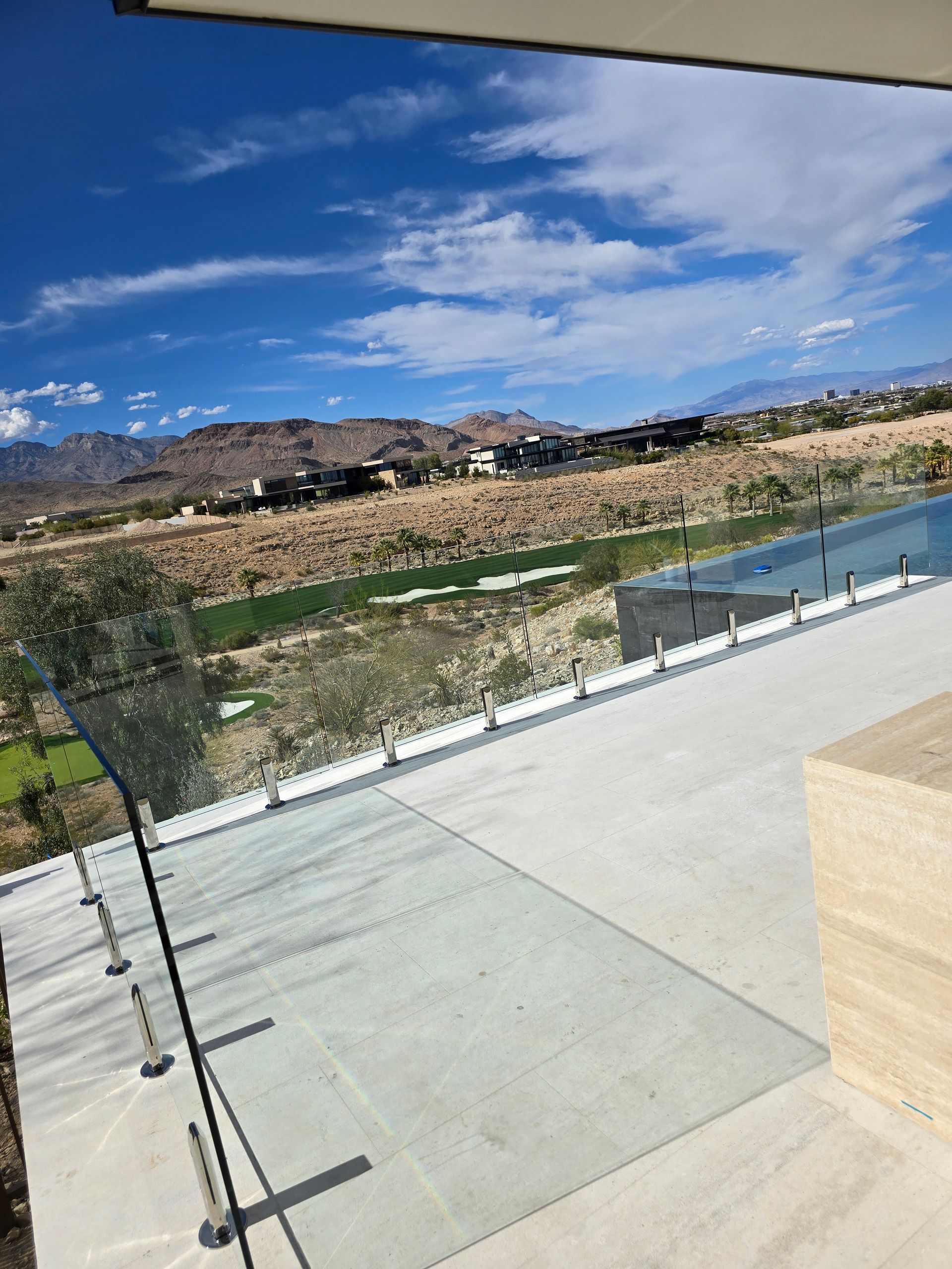 Patio overlooking a rocky hillside, blue sky, and a narrow reflecting pool beside a glass railing.
