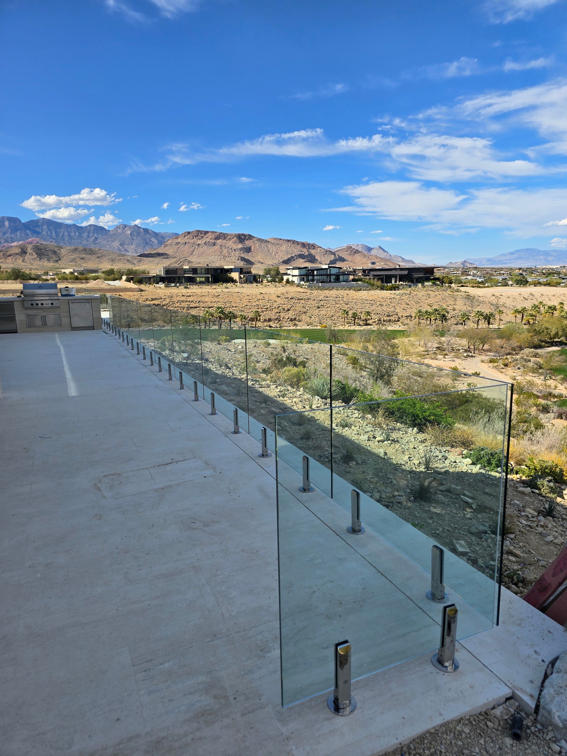 Concrete terrace with glass railing overlooking a rocky desert valley and distant mountains under a blue sky