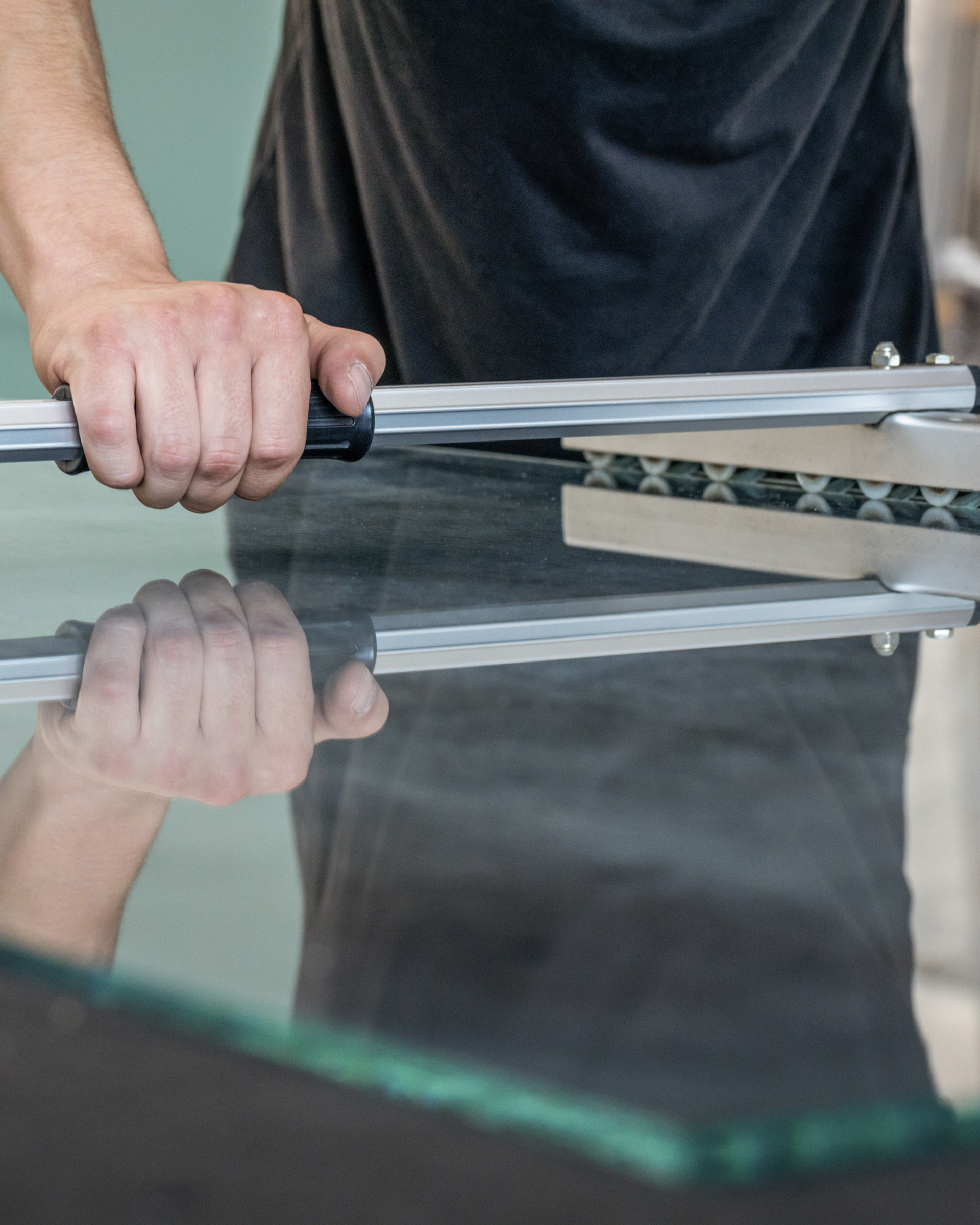 Person cutting glass with a tool over a reflective glass surface