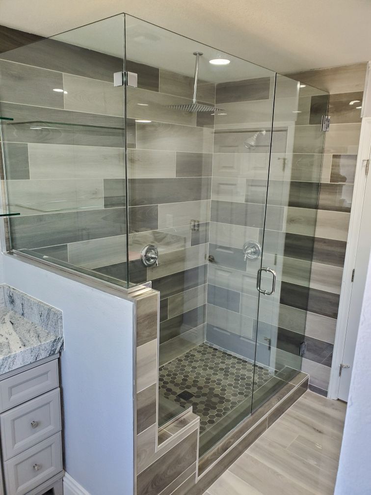 Modern bathroom with a glass-enclosed shower, gray tile walls, and light wood flooring.