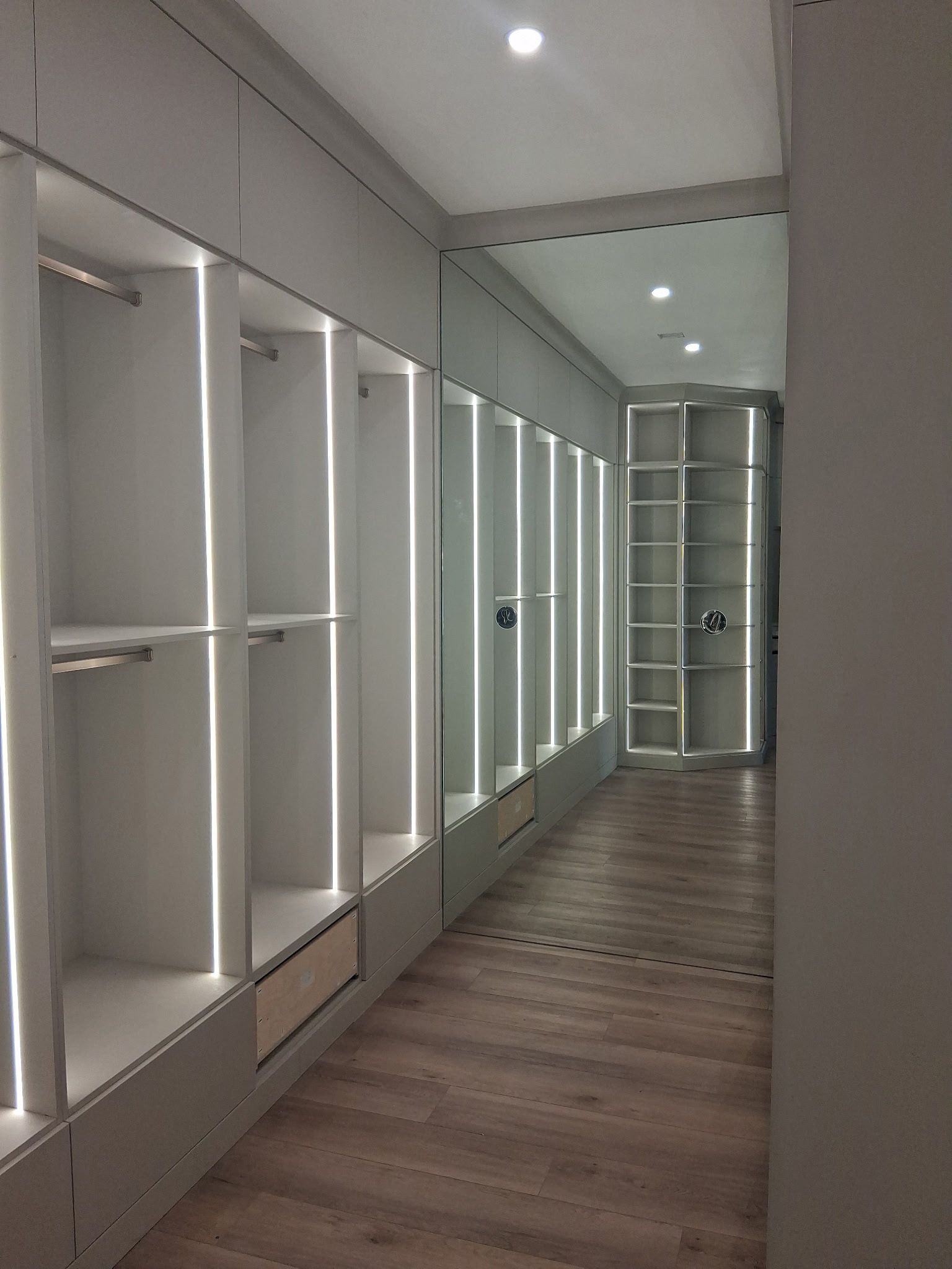 Empty modern hallway with built-in white cabinets, wood floor, and recessed ceiling lights.
